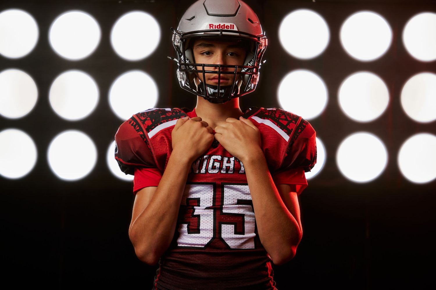 Close-up shot of football player in red jersey and helmet with focused expression against spotlight backdrop.