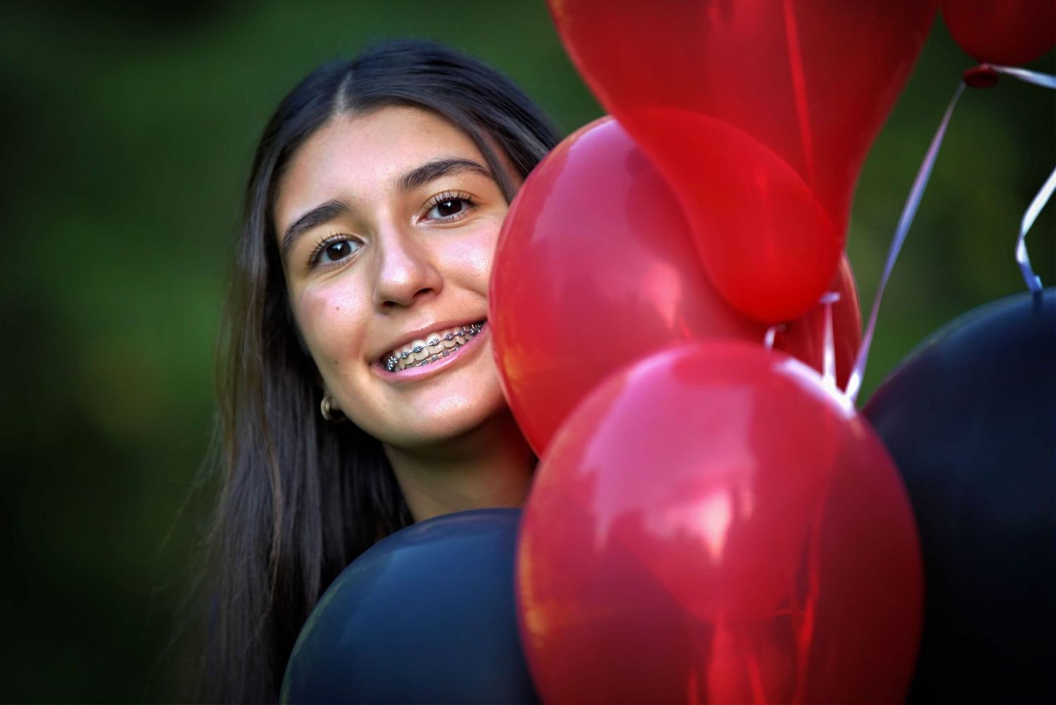 A person stands by red heart-shaped balloons with dark trees and evening sky in the background.