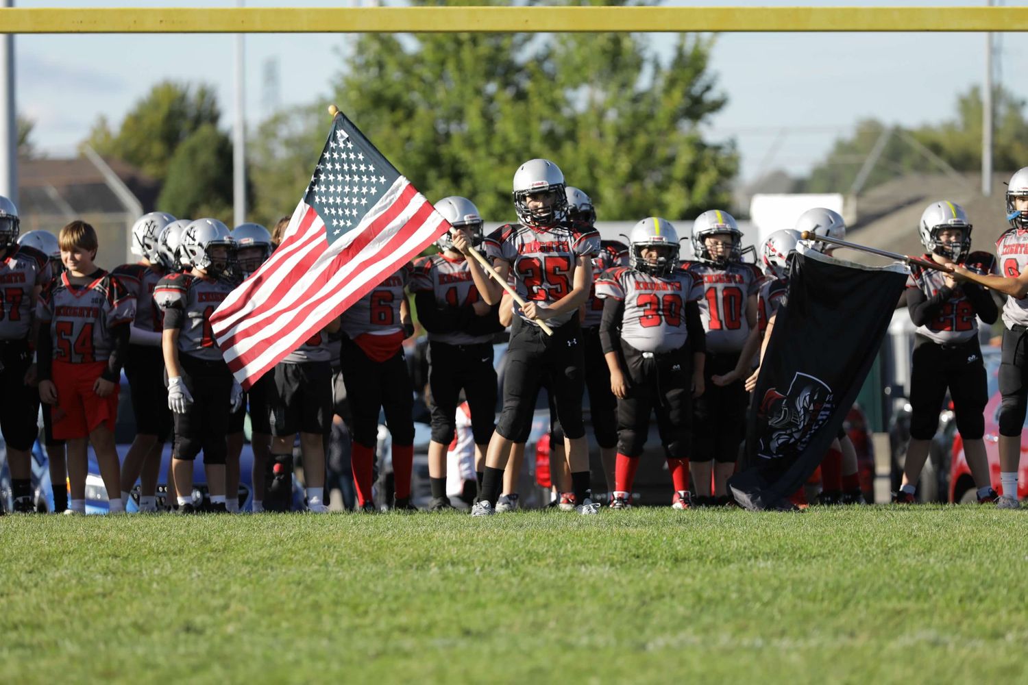 American football teams face off on a sunny field as fans wave US flags on the sidelines during a game.