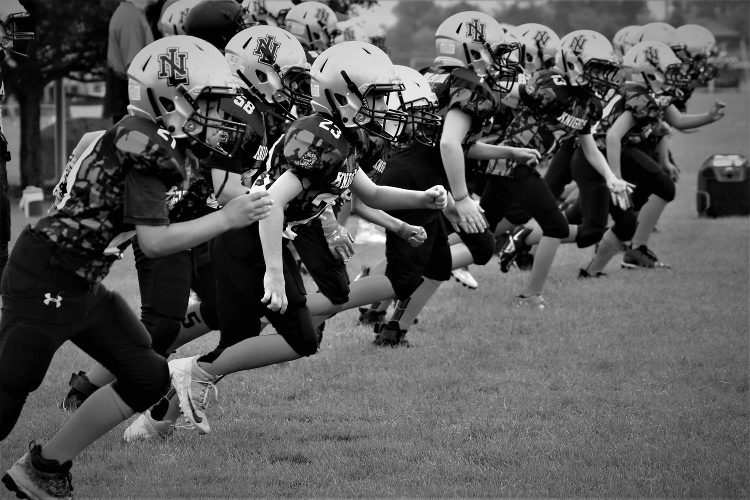 Black and white action shot of football players lined up in defensive formation on field.