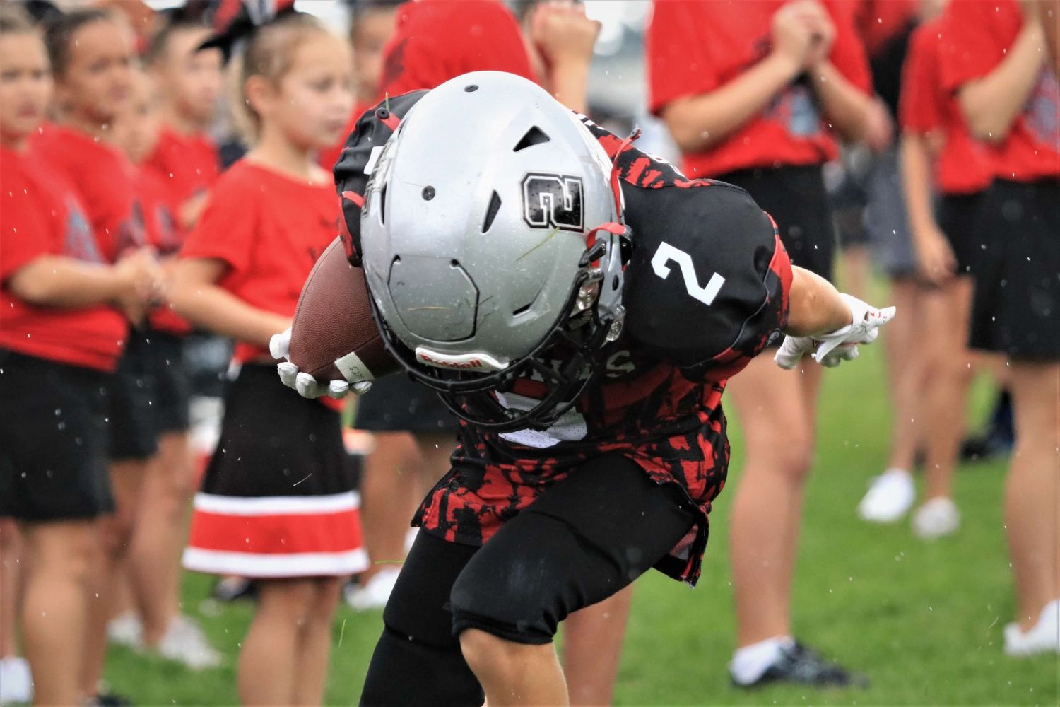 Football players and cheerleaders line up in formation on a grass field during team practice or pregame activities.