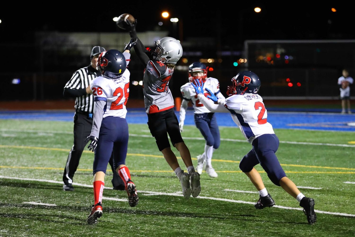 Football players compete for the ball during a nighttime game on an illuminated field.