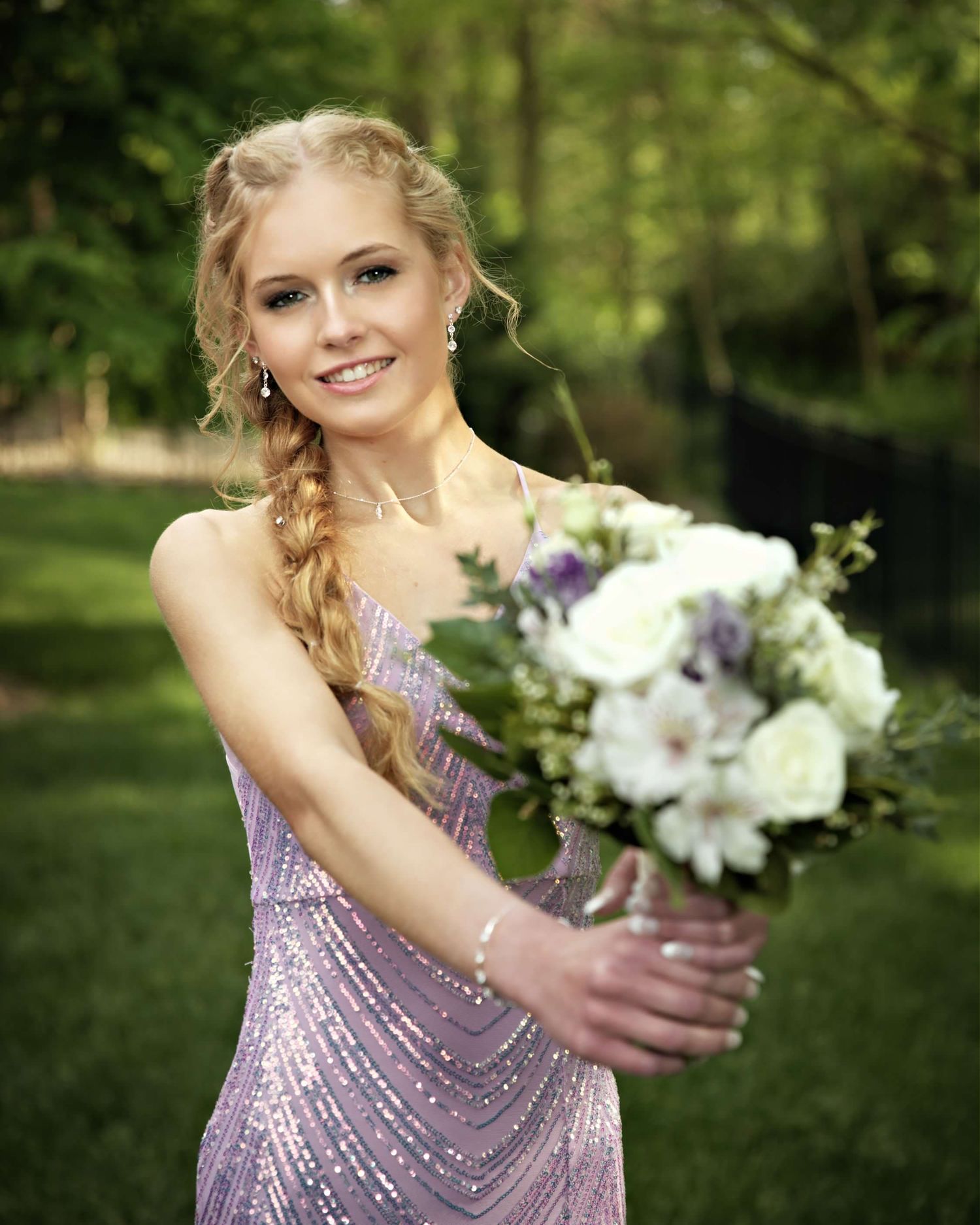 A person in a sparkly lavender dress poses outdoors with a white floral bouquet.