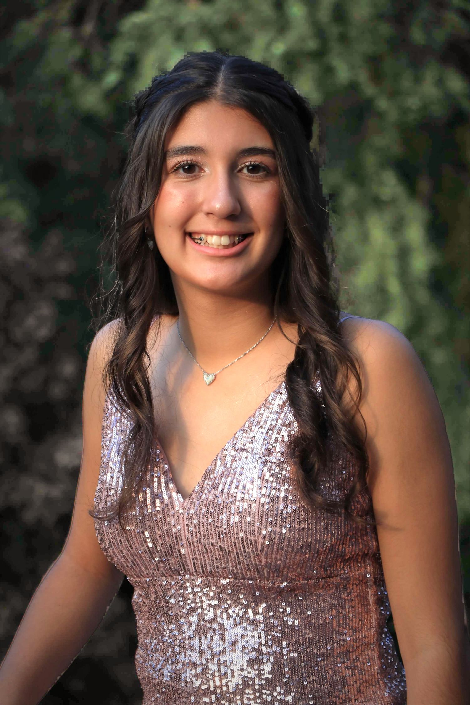 Portrait of someone wearing a sparkly sequined dress standing outside against green foliage background.