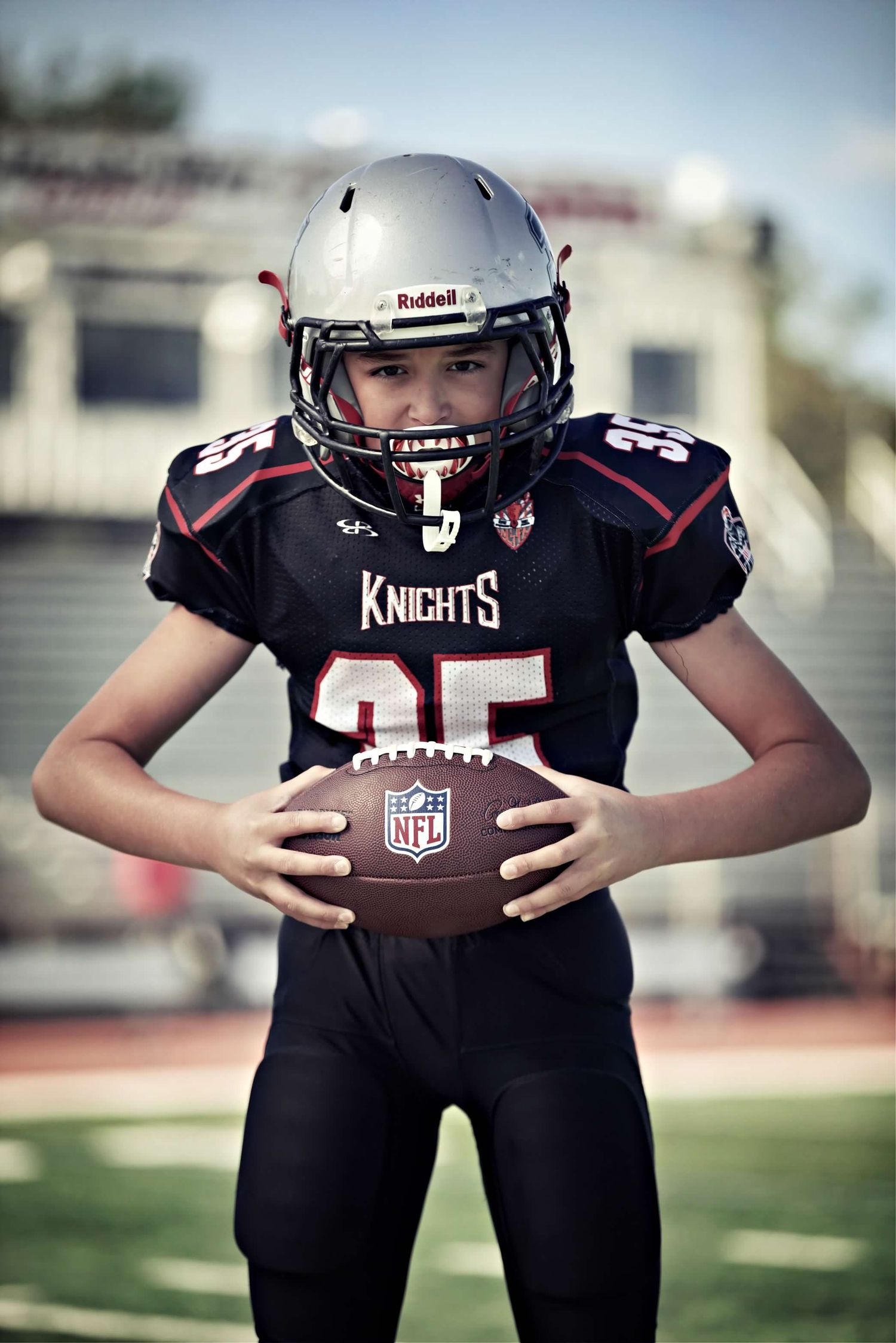 Young football player in Knights uniform number 35 posing with NFL football on field.