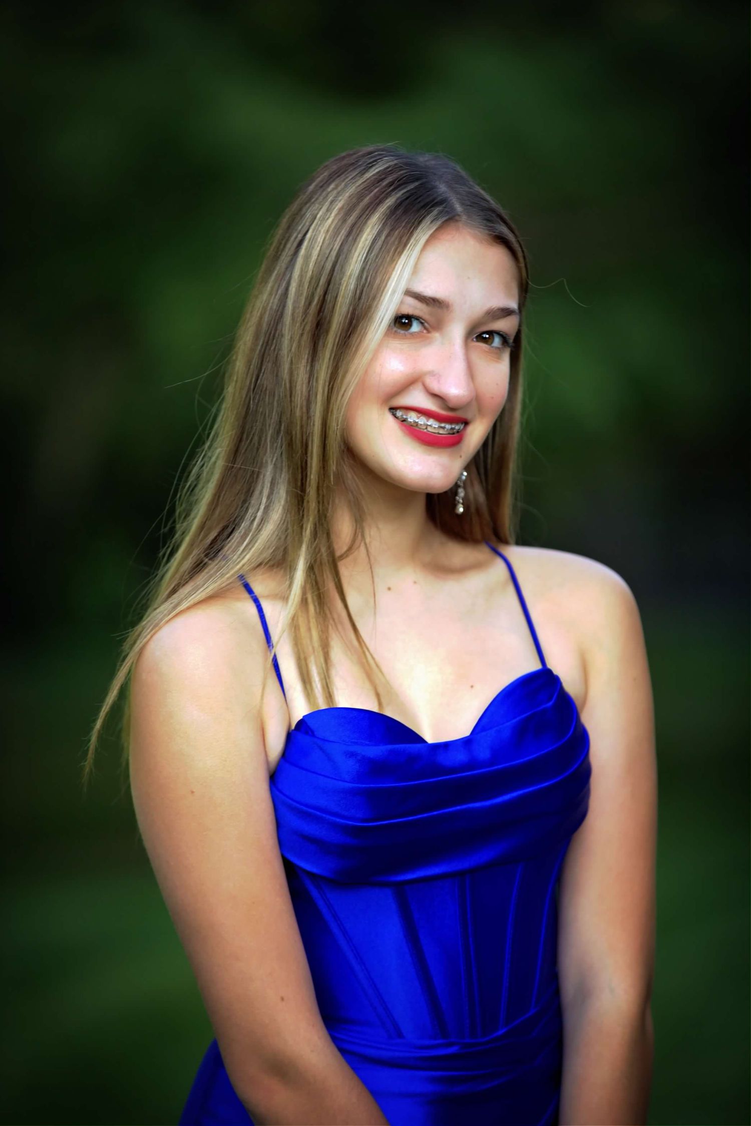 A portrait of someone wearing a royal blue formal dress against a blurred green outdoor background.