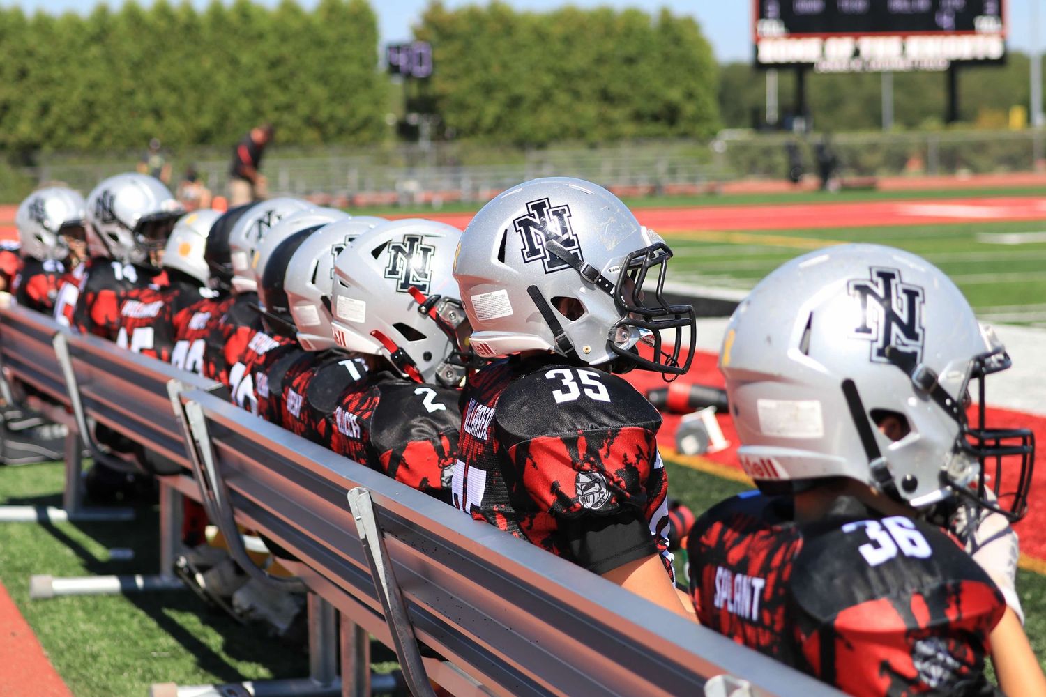 Football helmets and equipment lined up on metal benches at a sports field during a game or practice session.