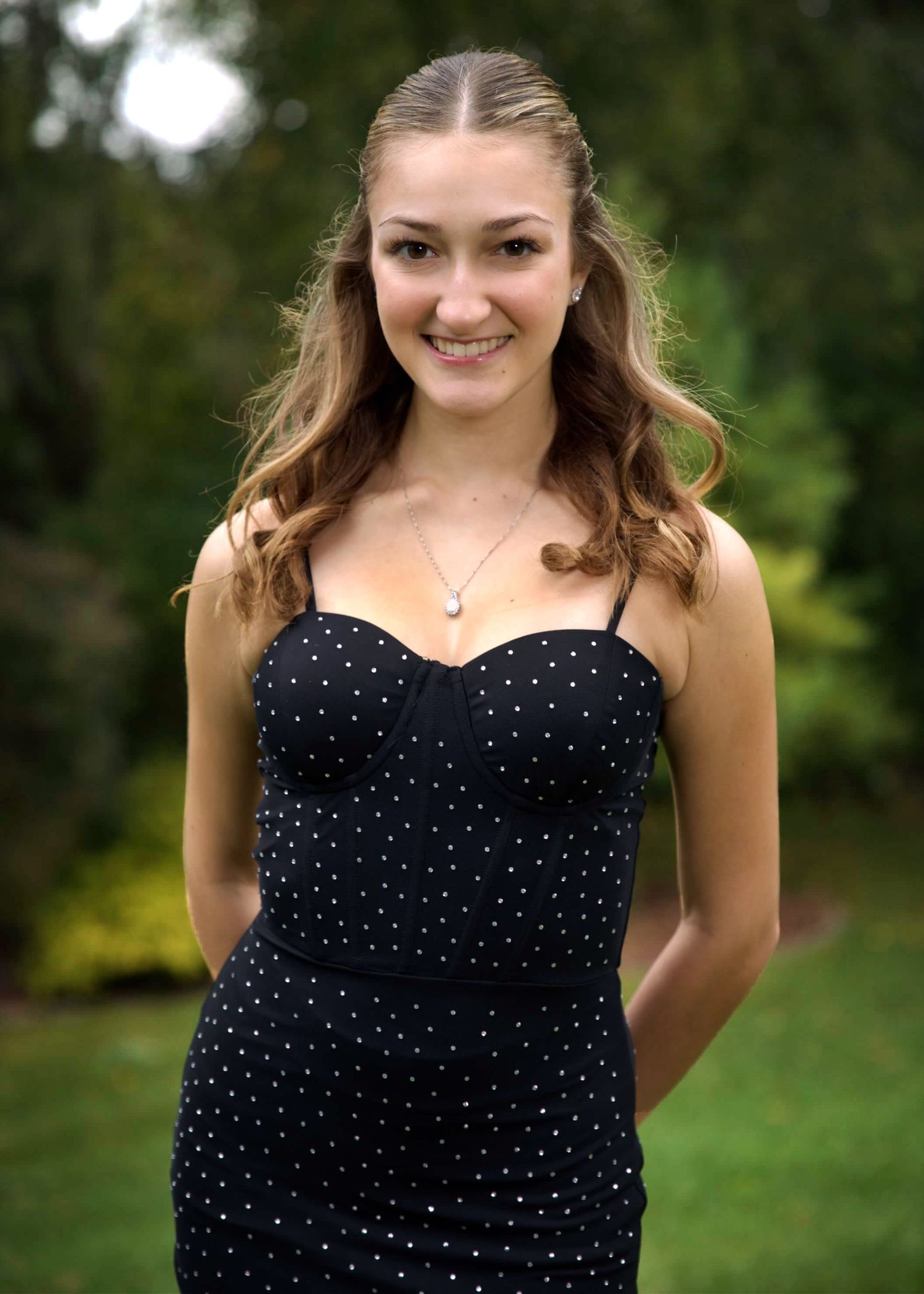 A person wearing a navy polka dot dress poses outdoors against a green natural background.
