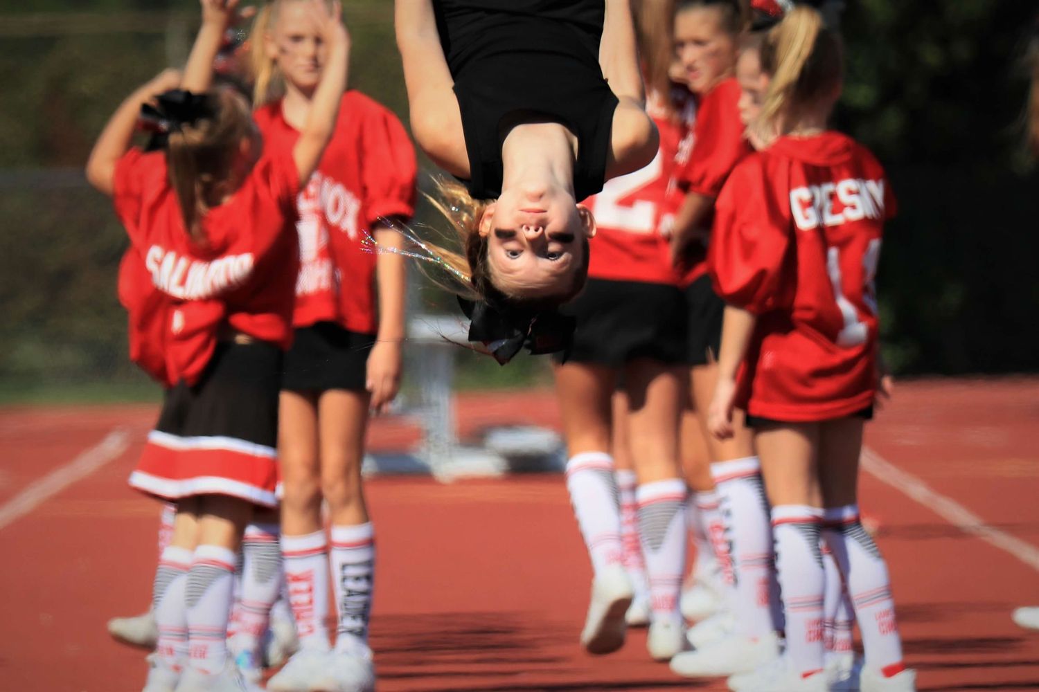 Cheerleaders perform synchronized moves during a school sporting event on the track field.