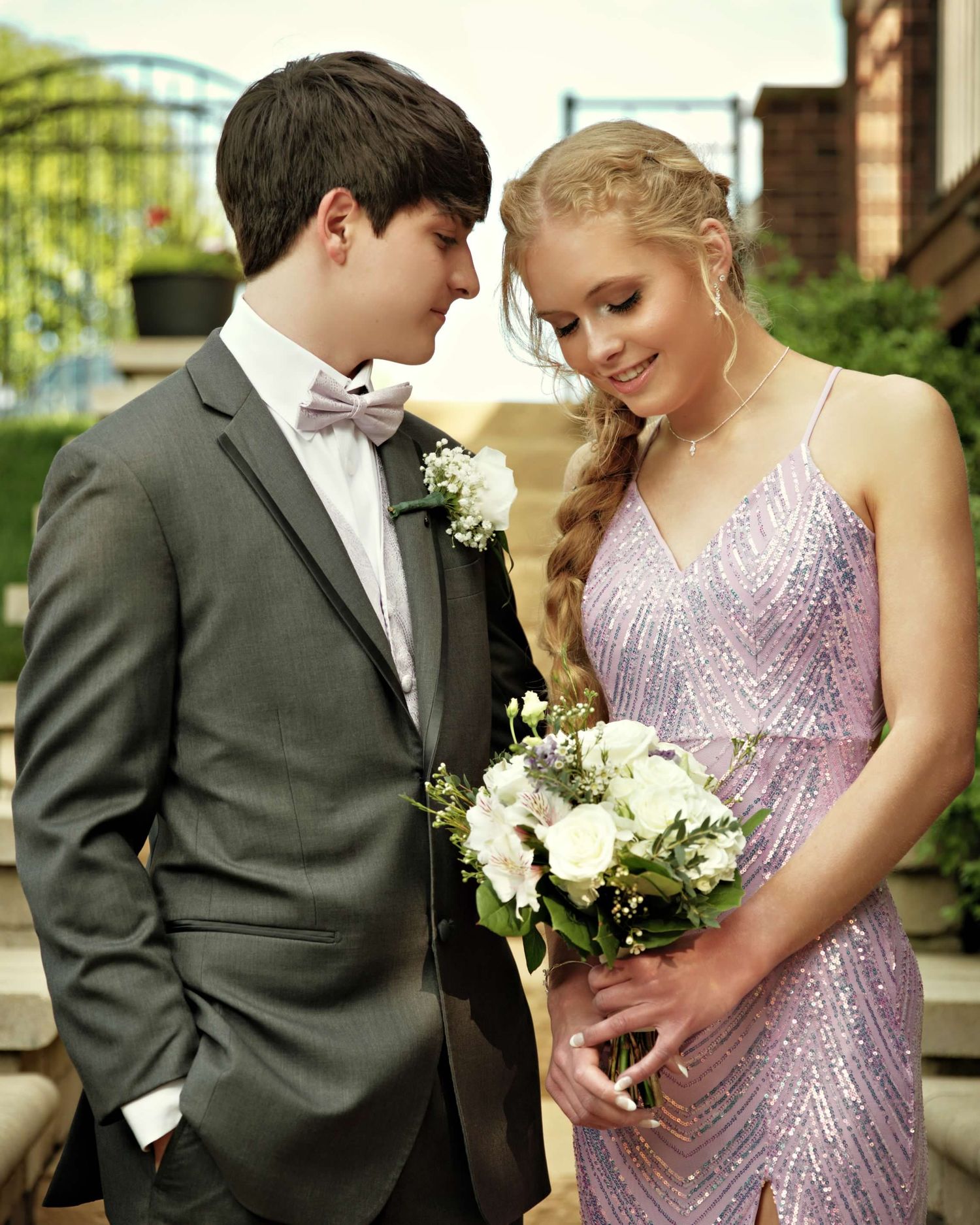 A couple shares a tender moment in formal attire with white flowers at an outdoor wedding celebration.