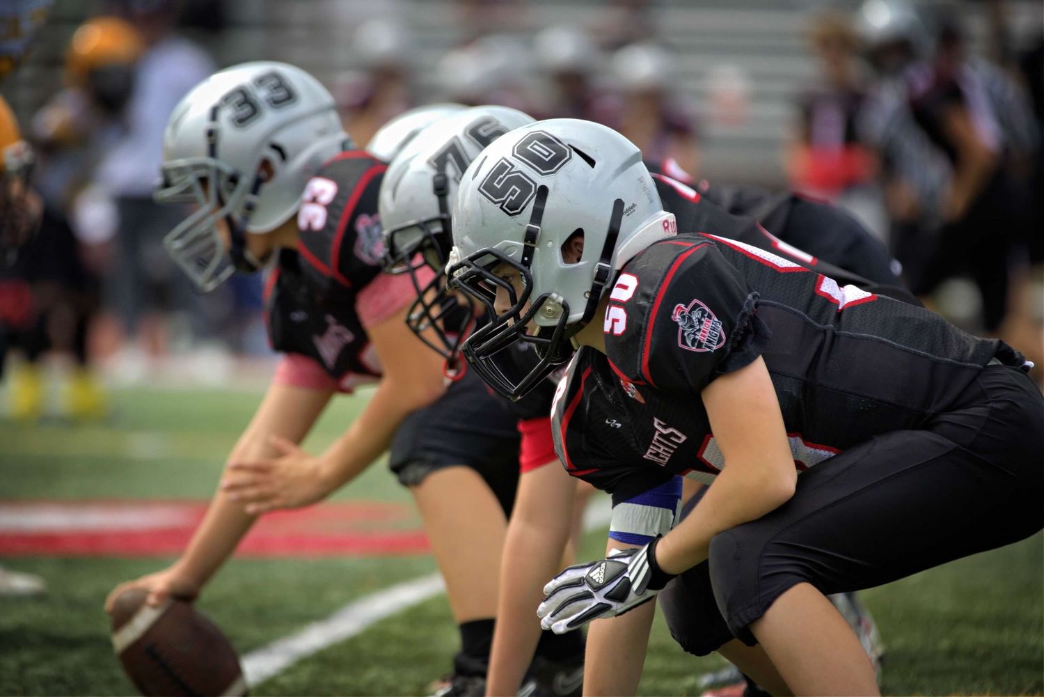 Football players in black uniforms lined up in formation during the snap count at the line of scrimmage during a game.