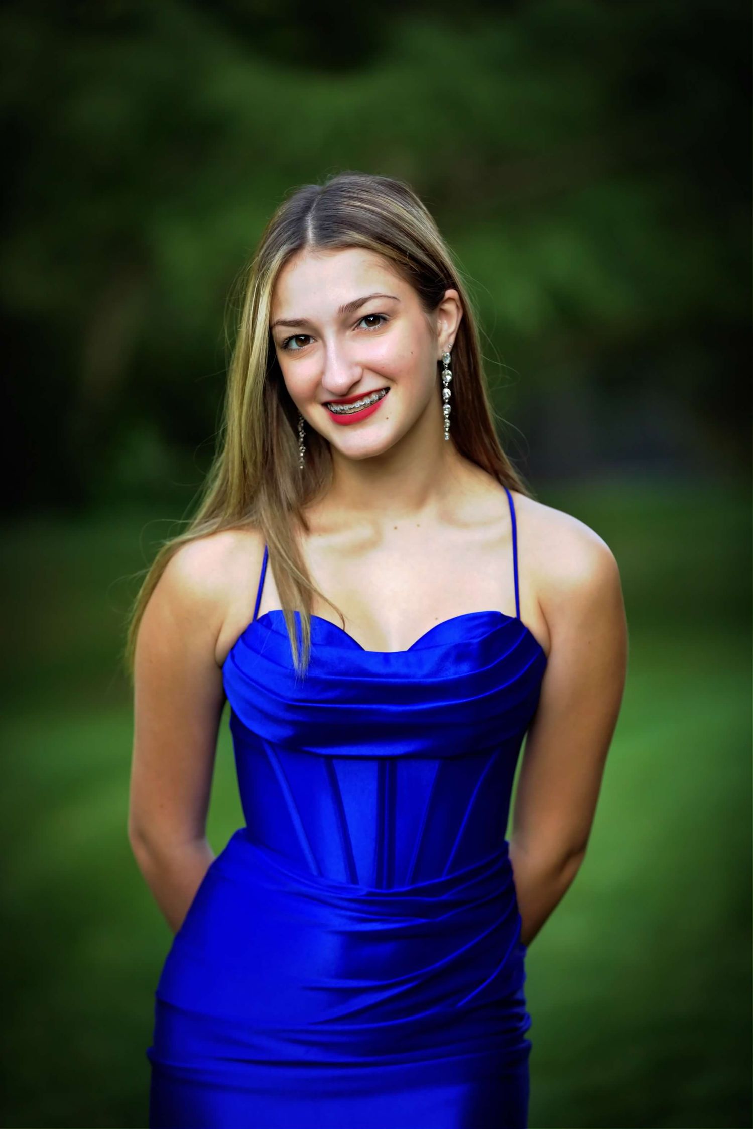 A sequence of playful poses in a royal blue formal dress with a natural green backdrop.