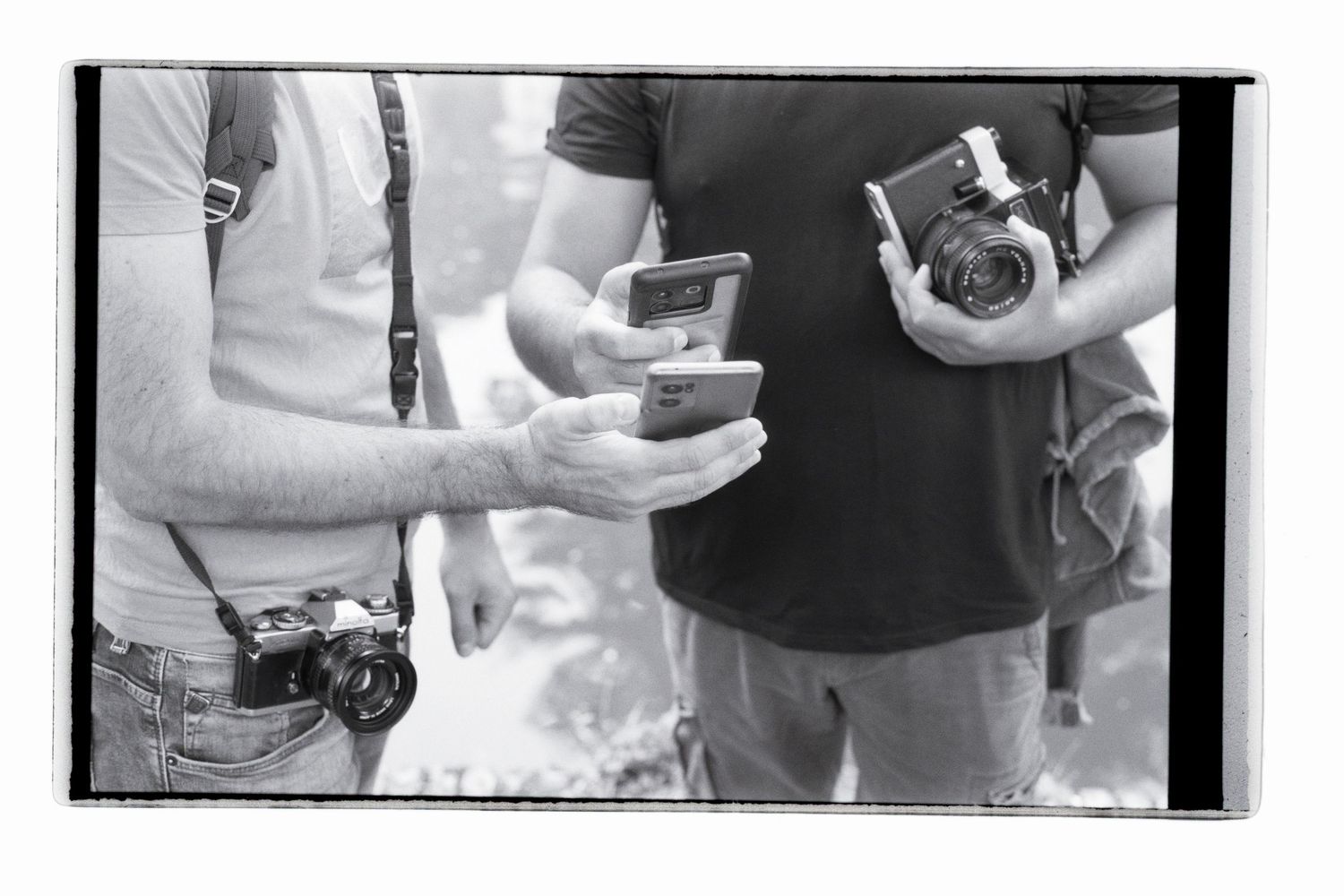 Two photographers share details on their phone, holding their old analog film cameras. Shot on black and white film.