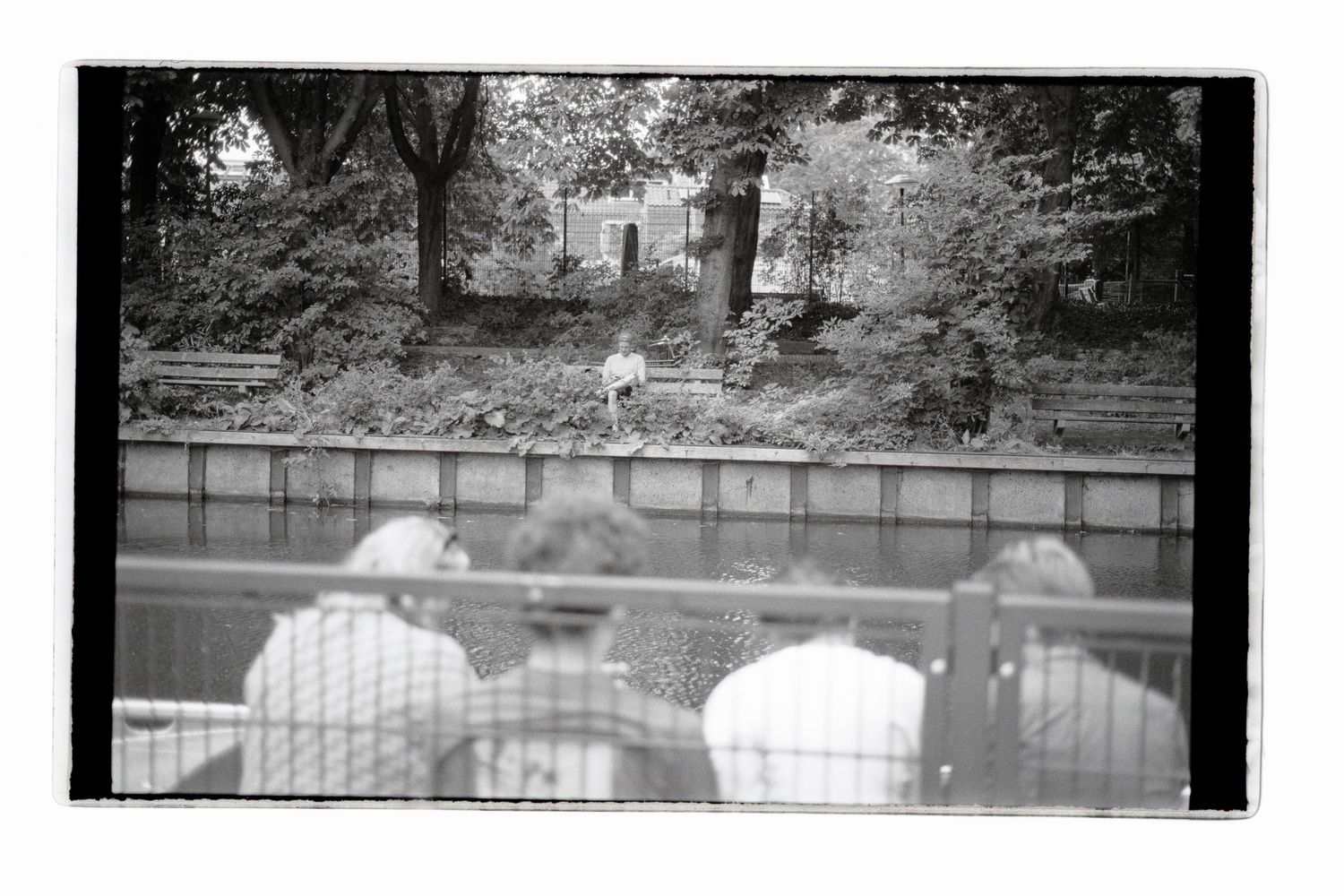Analog b&w shot with group of friends sitting on the waters edge, while on the other side of the river a single soul is reading a book.