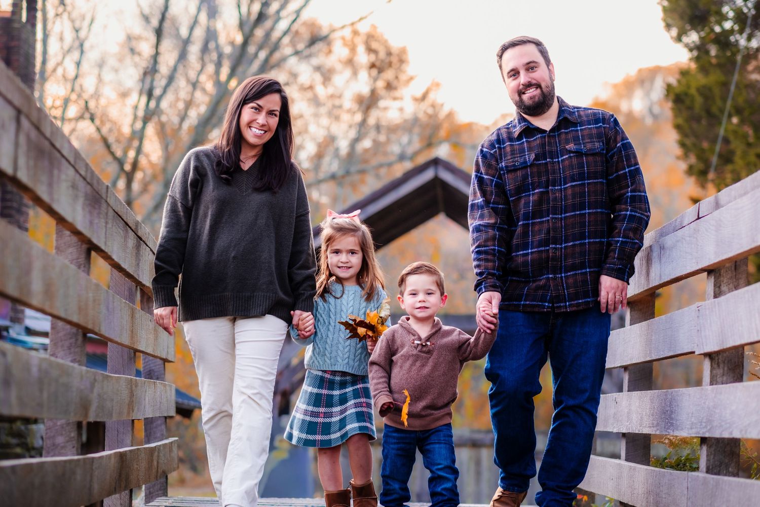Family of four posing on a wooden bridge surrounded by autumn foliage during a fall outdoor photo session.