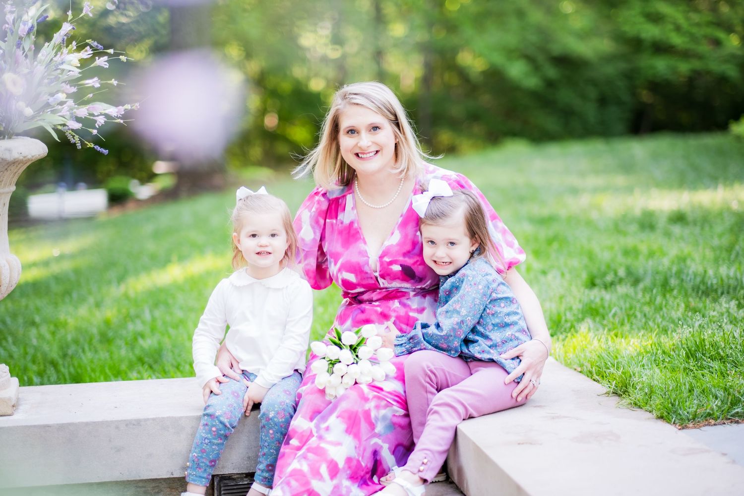 A family wearing pink and blue sits together on stone steps in a lush garden setting.