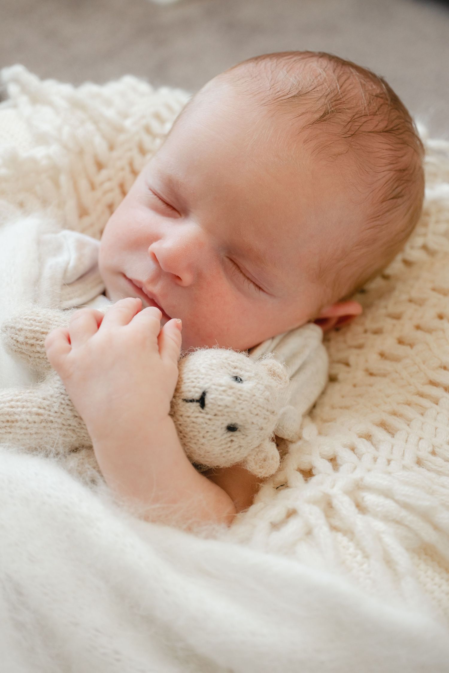 Peaceful newborn baby sleeping on white knit blanket while holding a small knitted bunny toy.