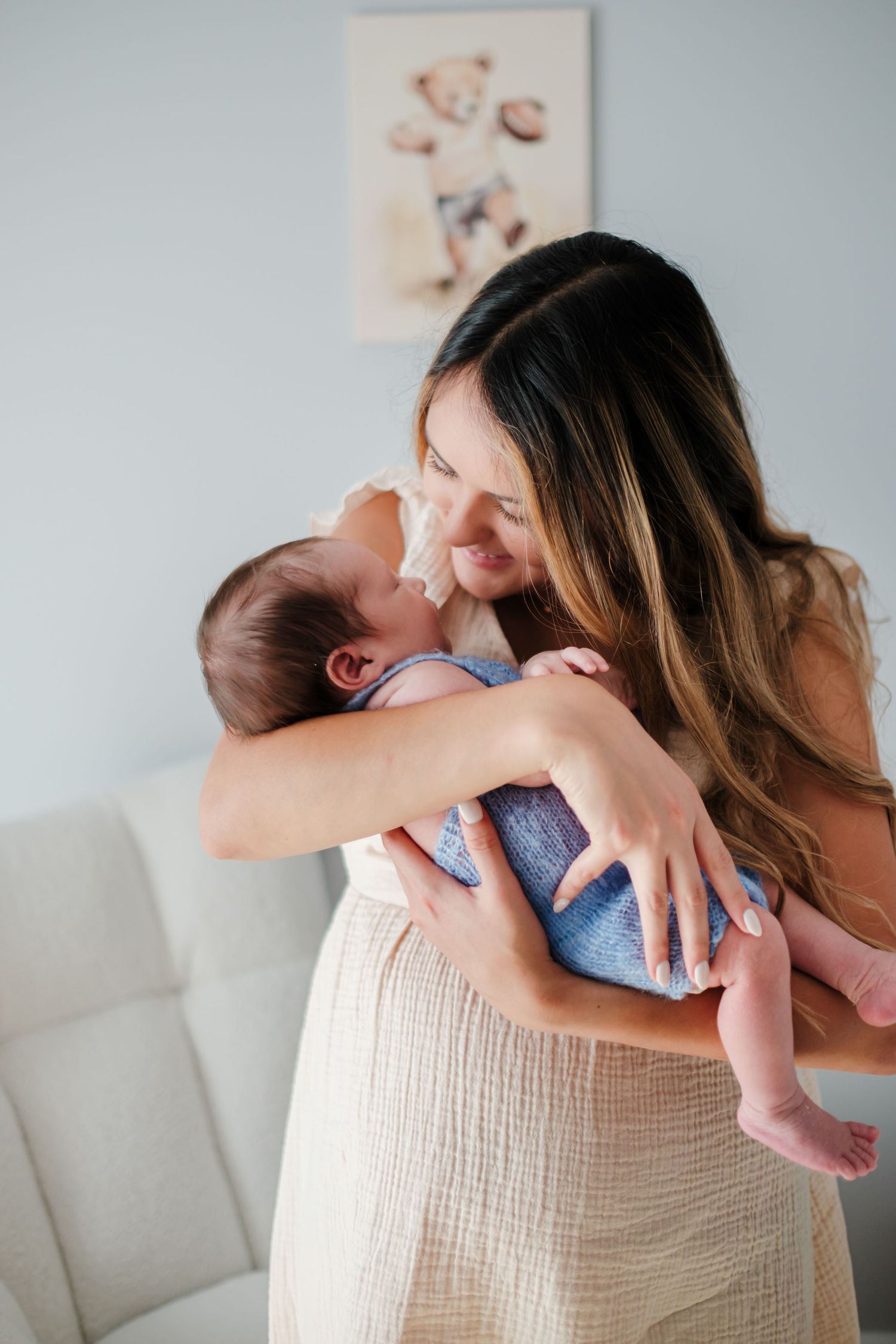 A loving mother tenderly holds her newborn baby close, smiling warmly in a soft, light-filled nursery room.