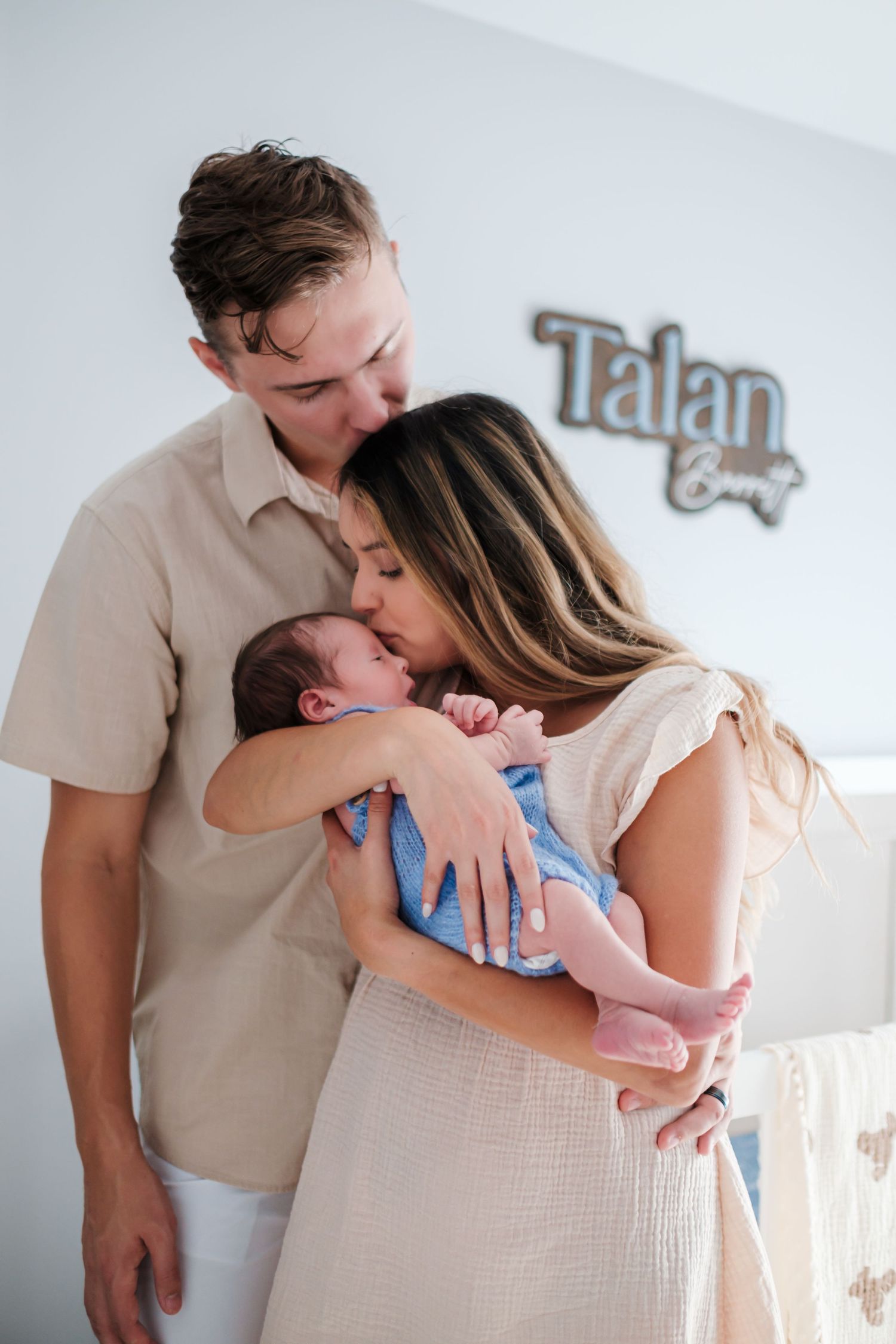 New parents kissing their newborn baby boy Talan in a nursery room.