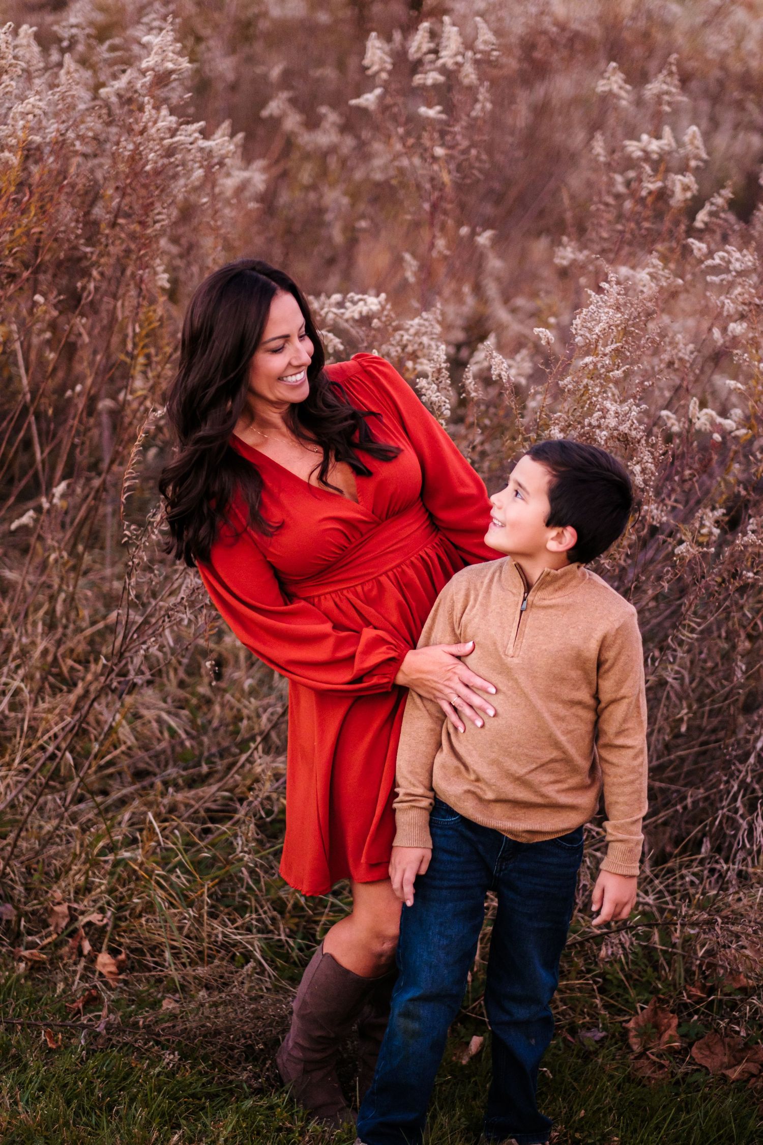 Woman in red dress and young boy sharing a joyful moment in a fall outdoor setting.