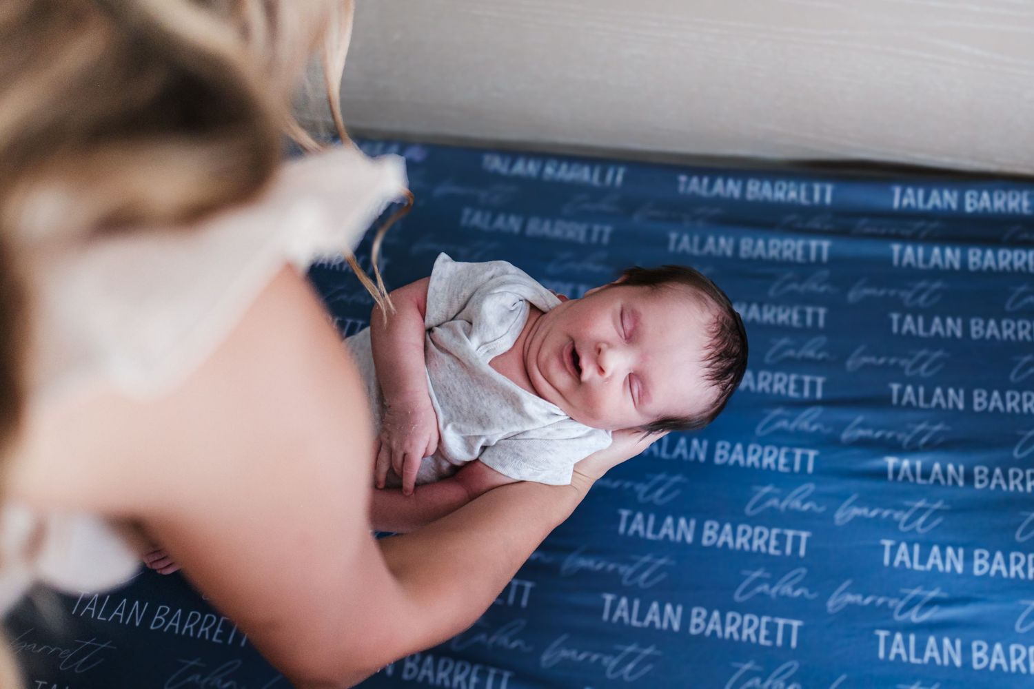 Newborn baby resting peacefully on a Talan Barrett branded blue blanket while being held by a parent.