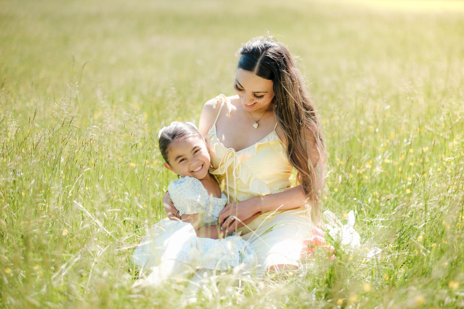 A couple relaxes together in a sunlit meadow filled with tall grass and wildflowers on a bright summer day.