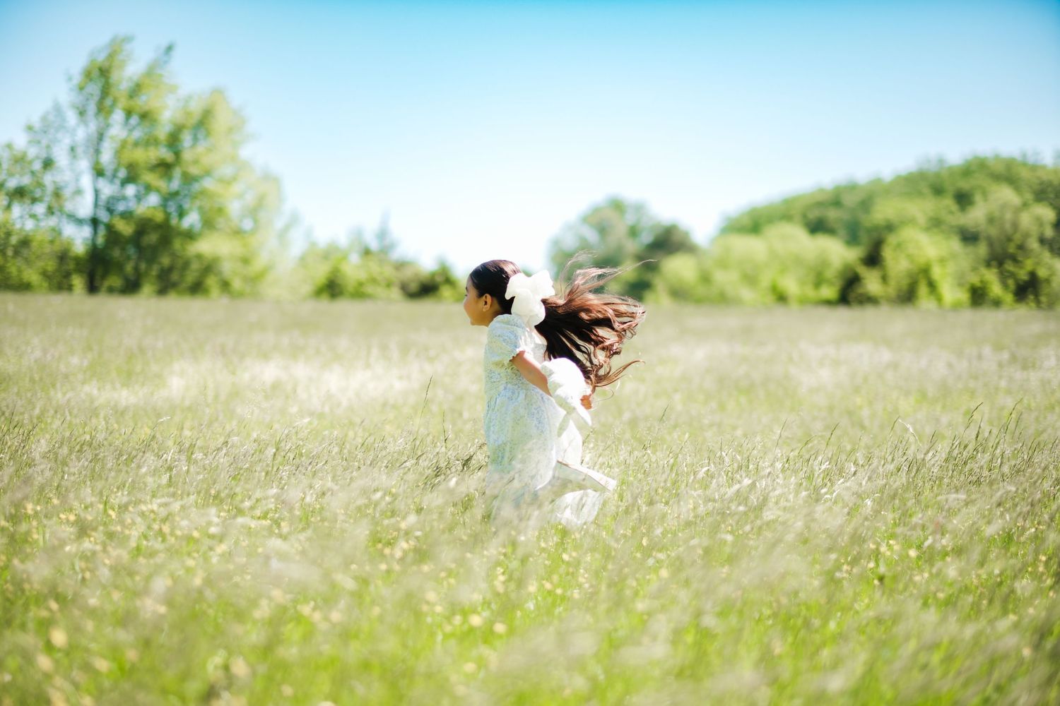 A young girl in a white dress twirls joyfully in a lush green meadow on a sunny summer day.