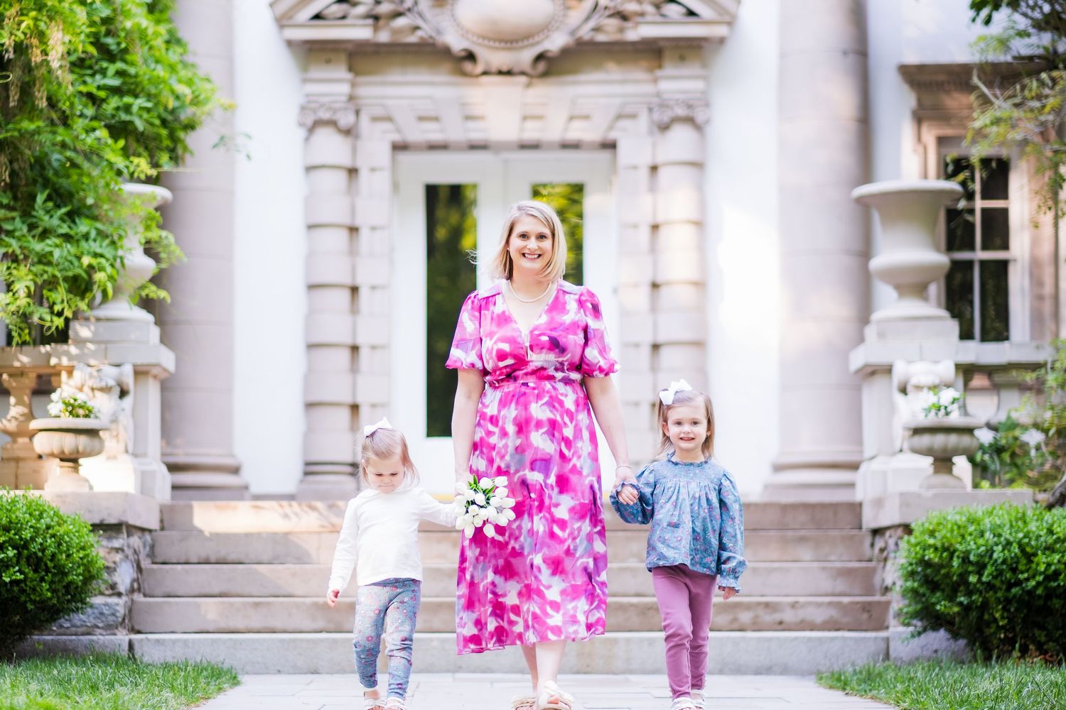 Family portrait session outside a grand stone building with classical columns and lush greenery in springtime.