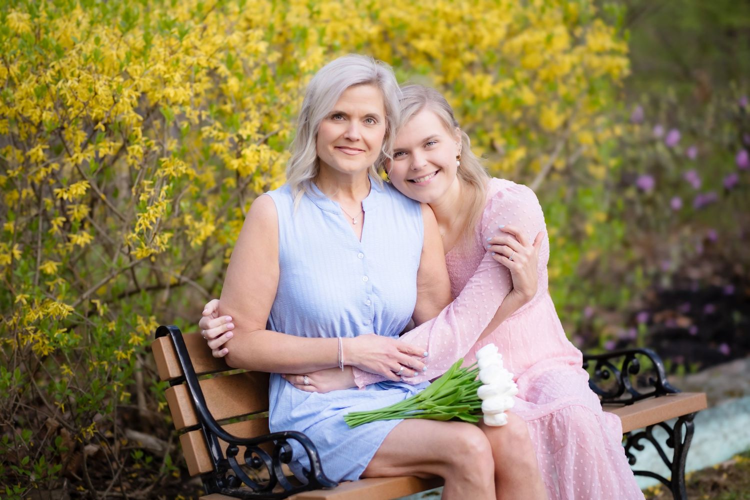 Two people sitting together on a bench in a garden with blooming yellow forsythia bushes in the background.