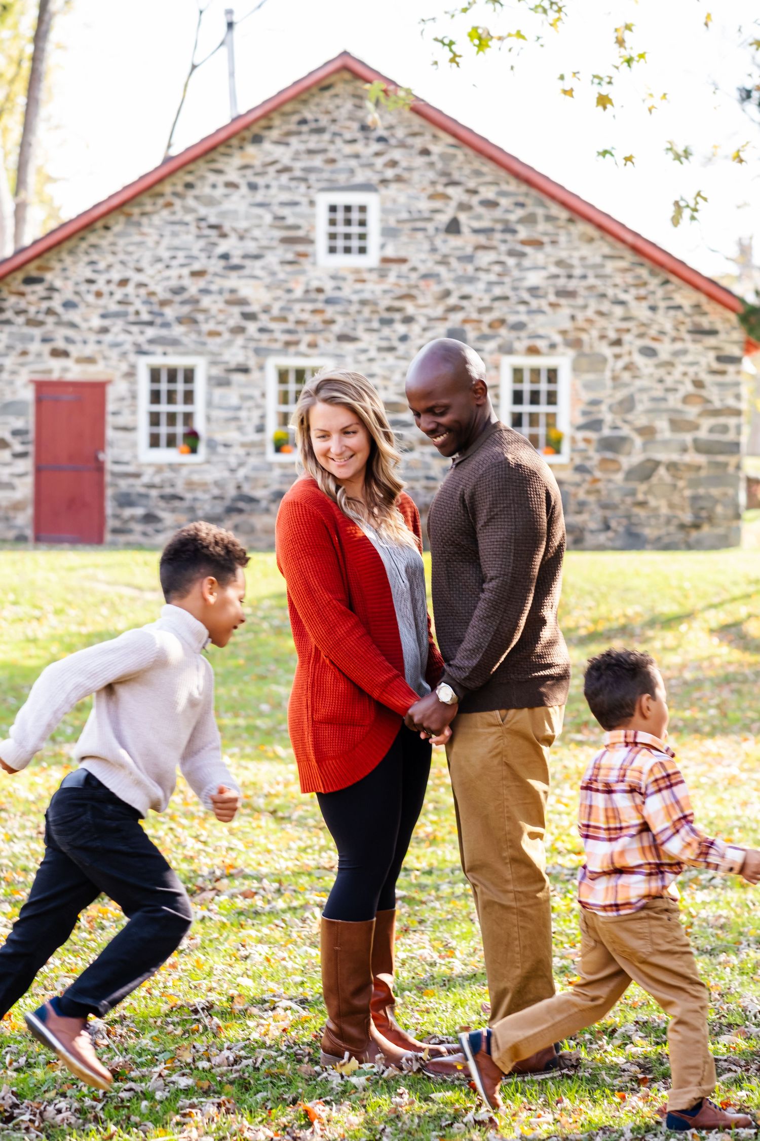 Interracial family with two young boys playing outdoors in front of a rustic stone house during autumn.