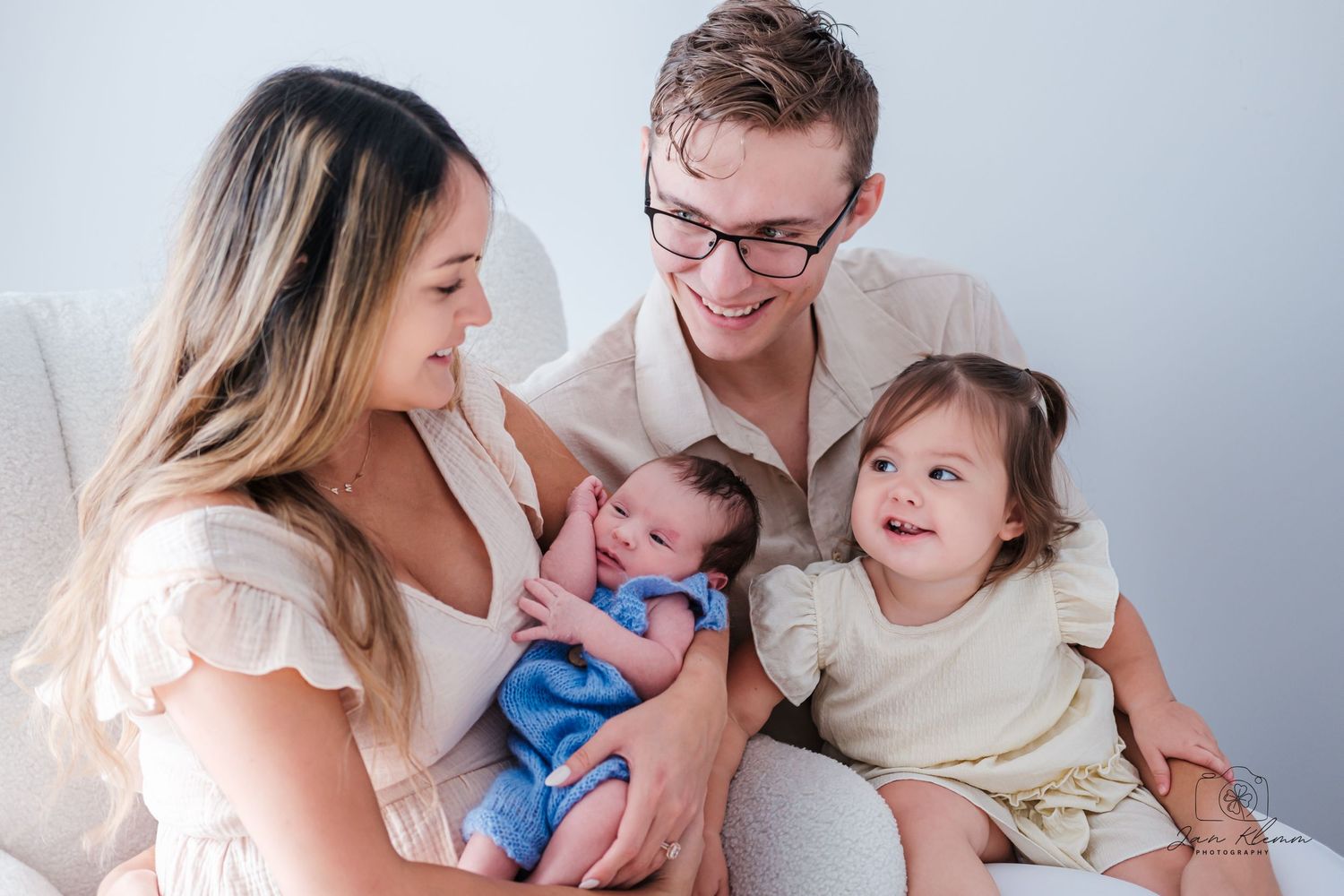 Happy family of four with newborn baby and toddler daughter posing together in a bright, airy studio photo.