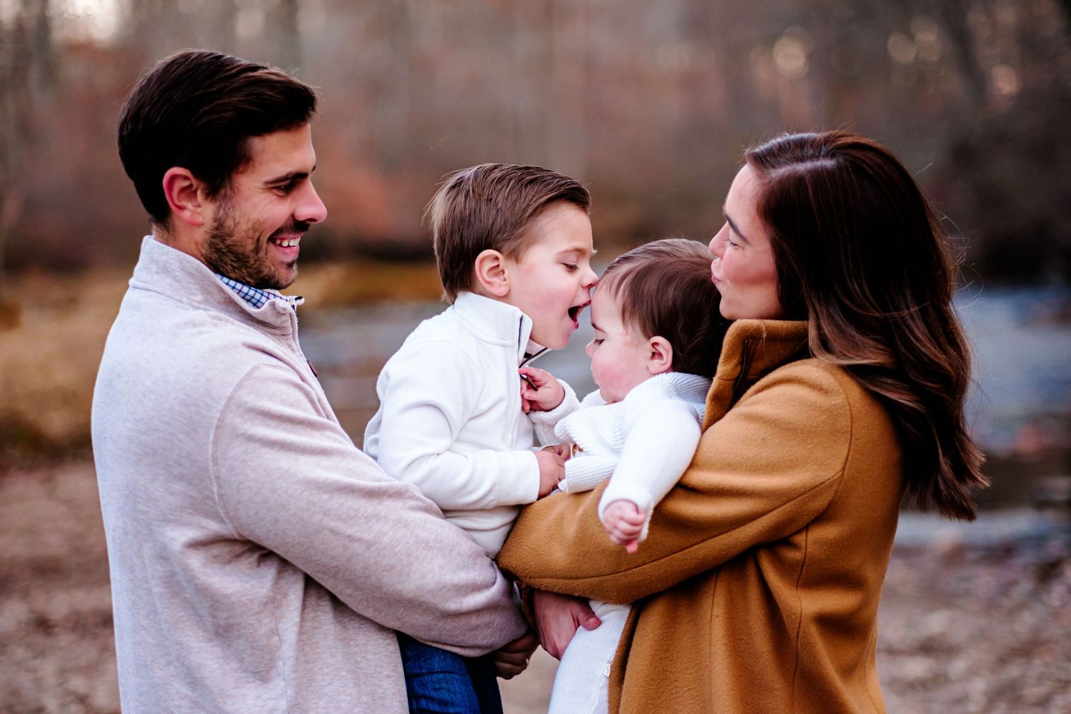 Happy family with two young children laughing outdoors in autumn, parents holding kids in a warm fall setting.