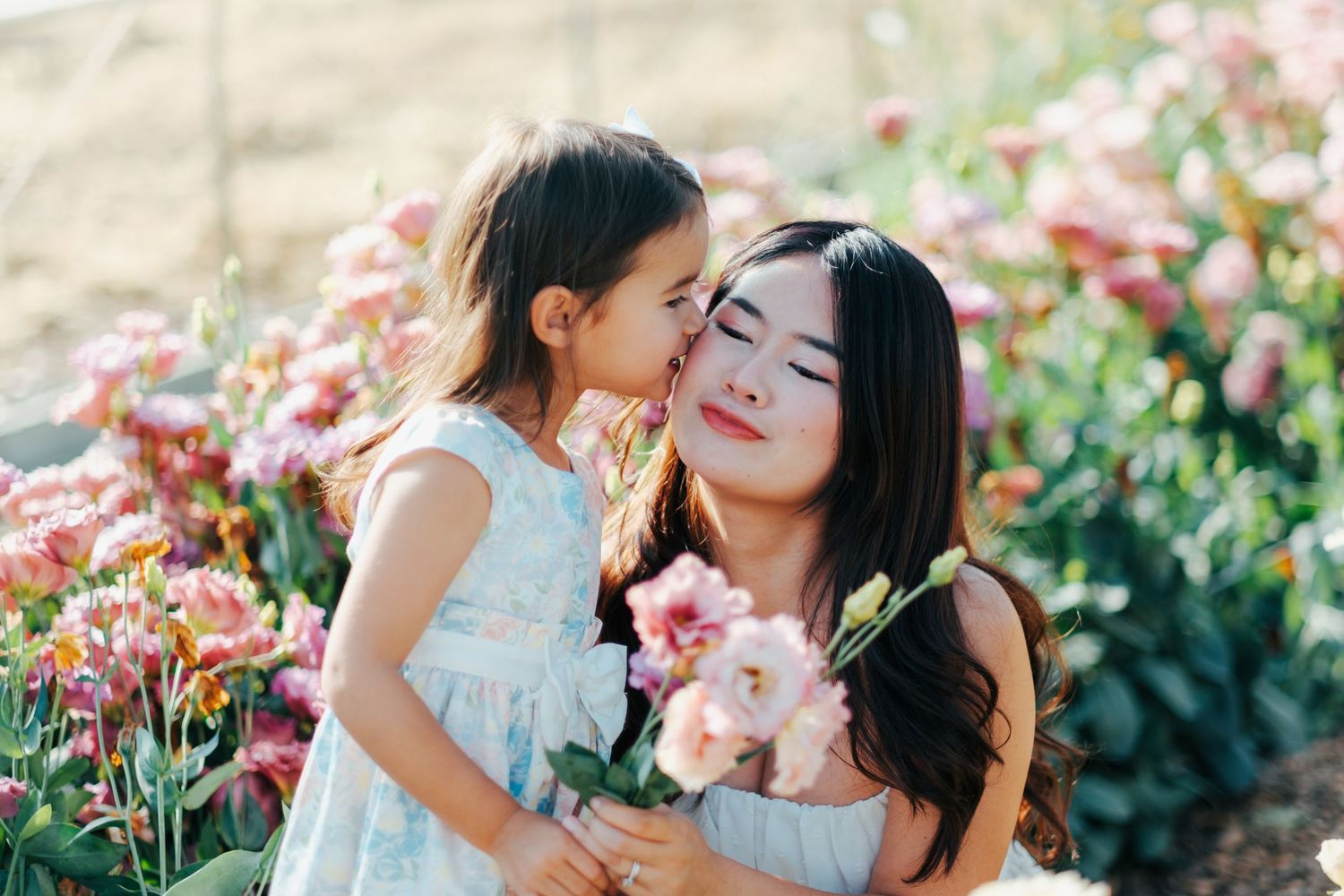 Two people share tender moments in a garden setting with pink flowers blooming in the background.