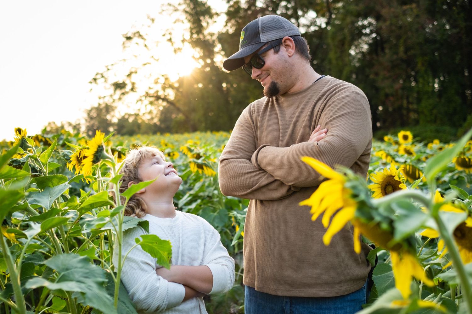 A father and child share a joyful moment in a sunflower field at golden hour, with the child looking up adoringly.