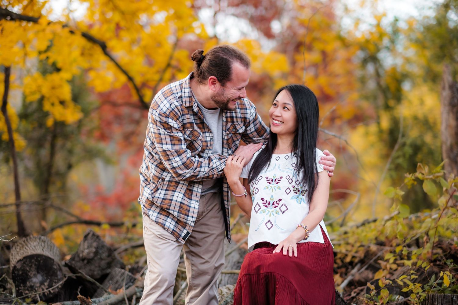 Couple sharing a romantic moment outdoors among vibrant autumn foliage in fall colors of red, orange, and yellow.