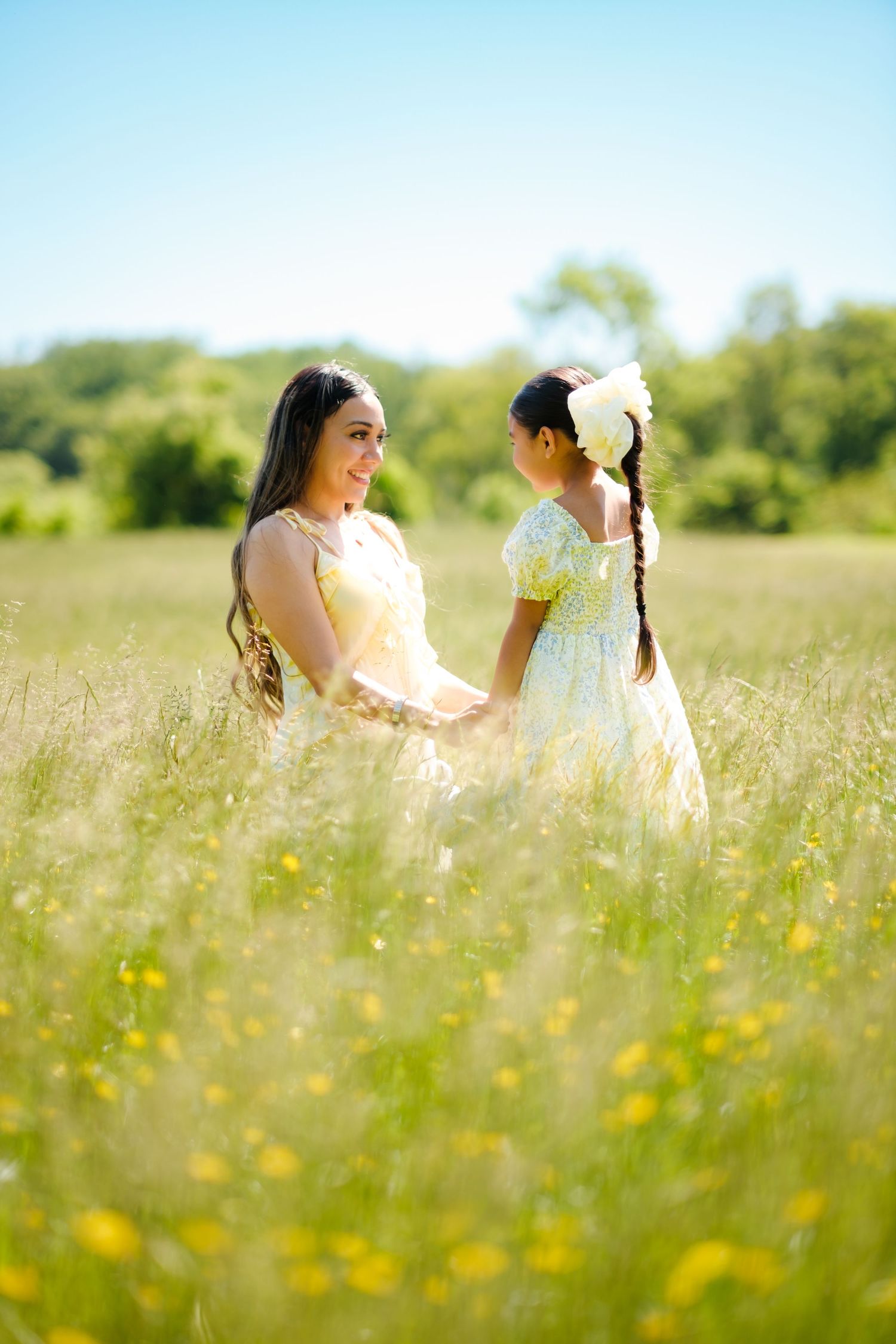 Mother and daughter in yellow dresses holding hands in a sunny wildflower meadow.