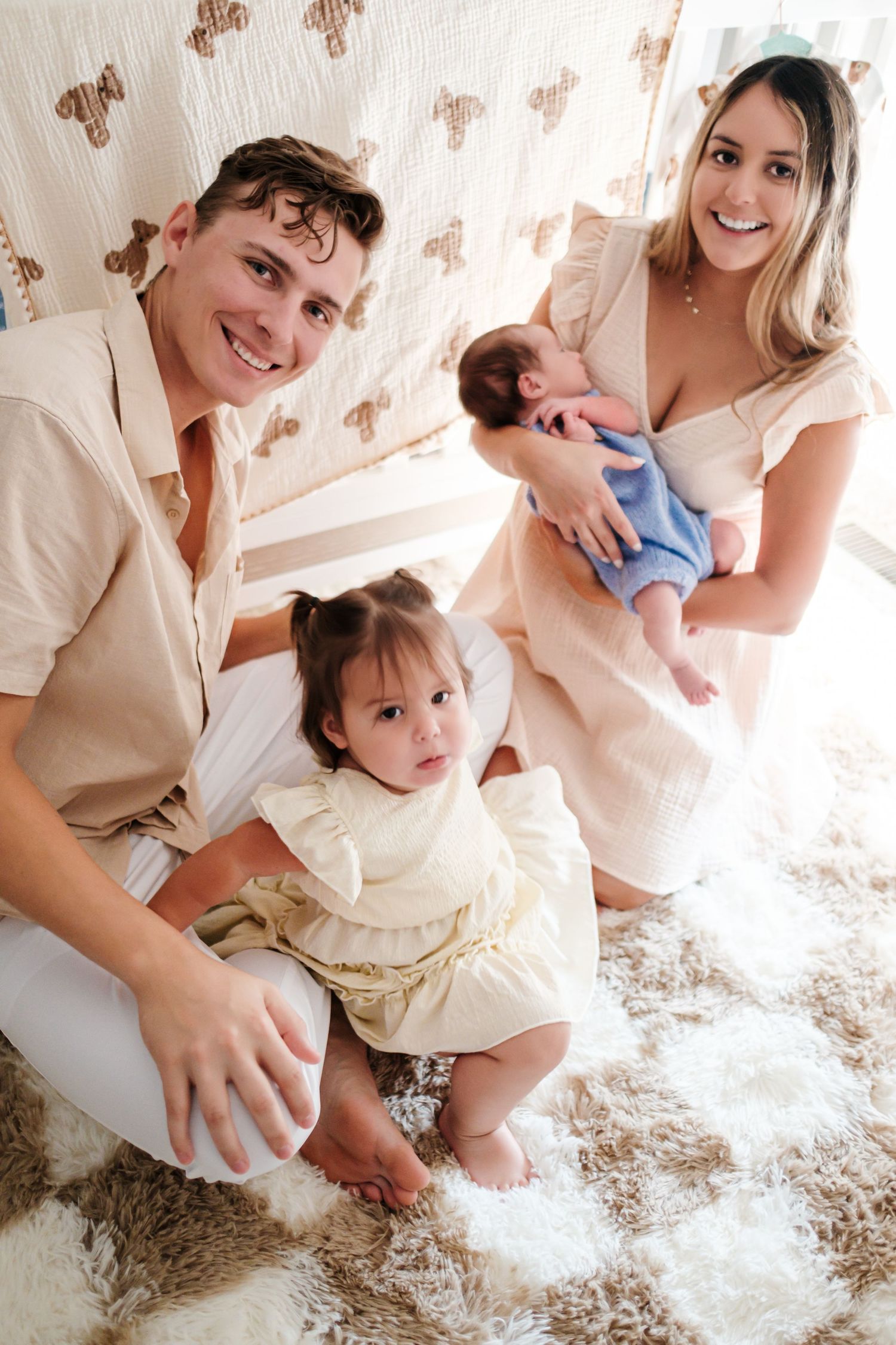Happy young family with toddler girl and newborn baby posing together on a fluffy rug.