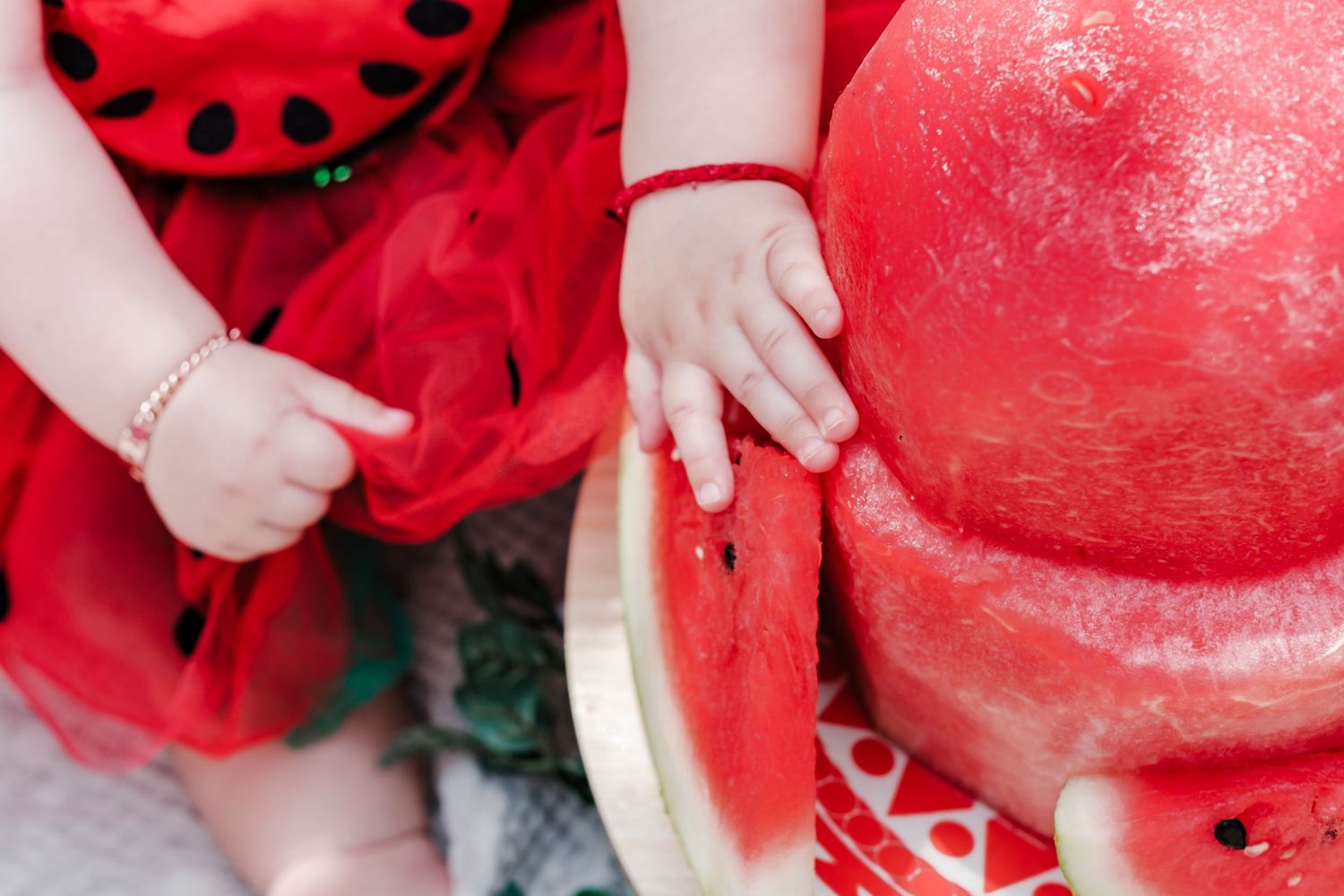 Baby in red ladybug costume touching fresh watermelon slices outdoors.
