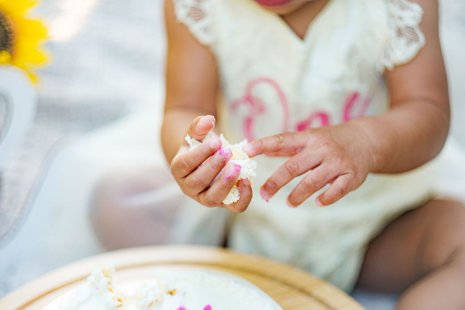 Close-up of baby hands holding smashed white birthday cake during first birthday cake smash.