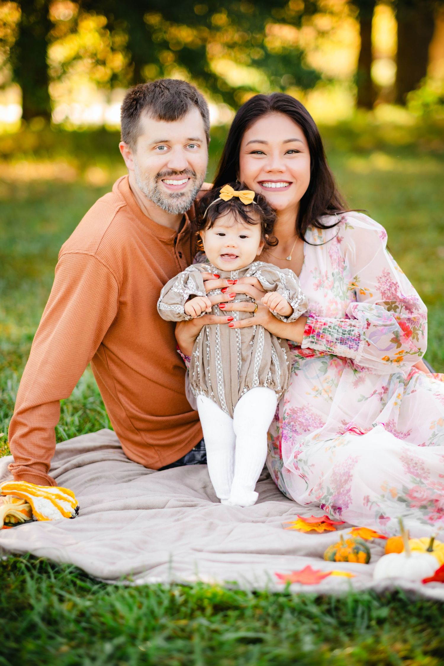 Happy family with baby girl enjoying autumn picnic on blanket in park with fall decorations.