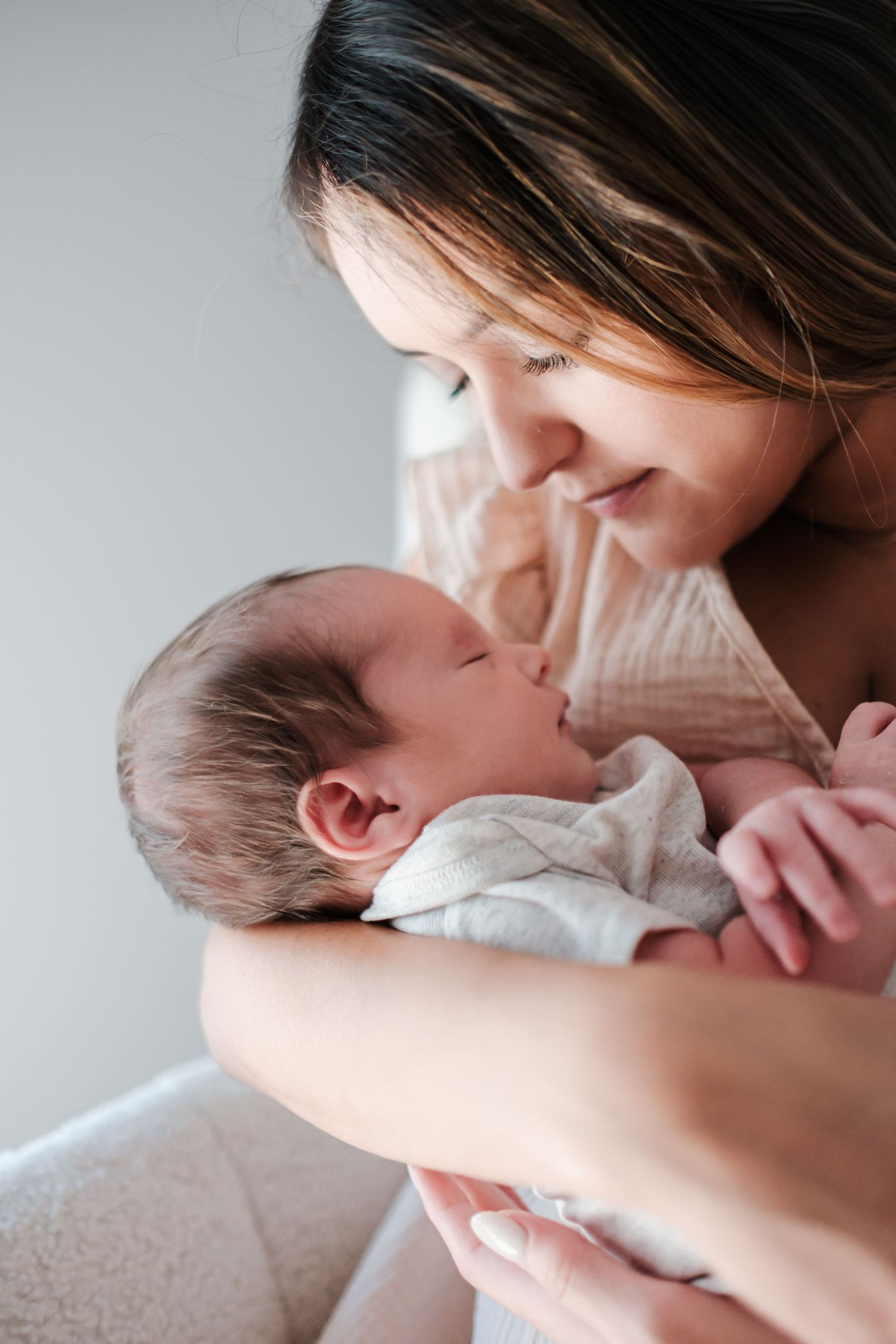 Close-up of a smiling mother tenderly holding her sleeping newborn baby wrapped in a white blanket.