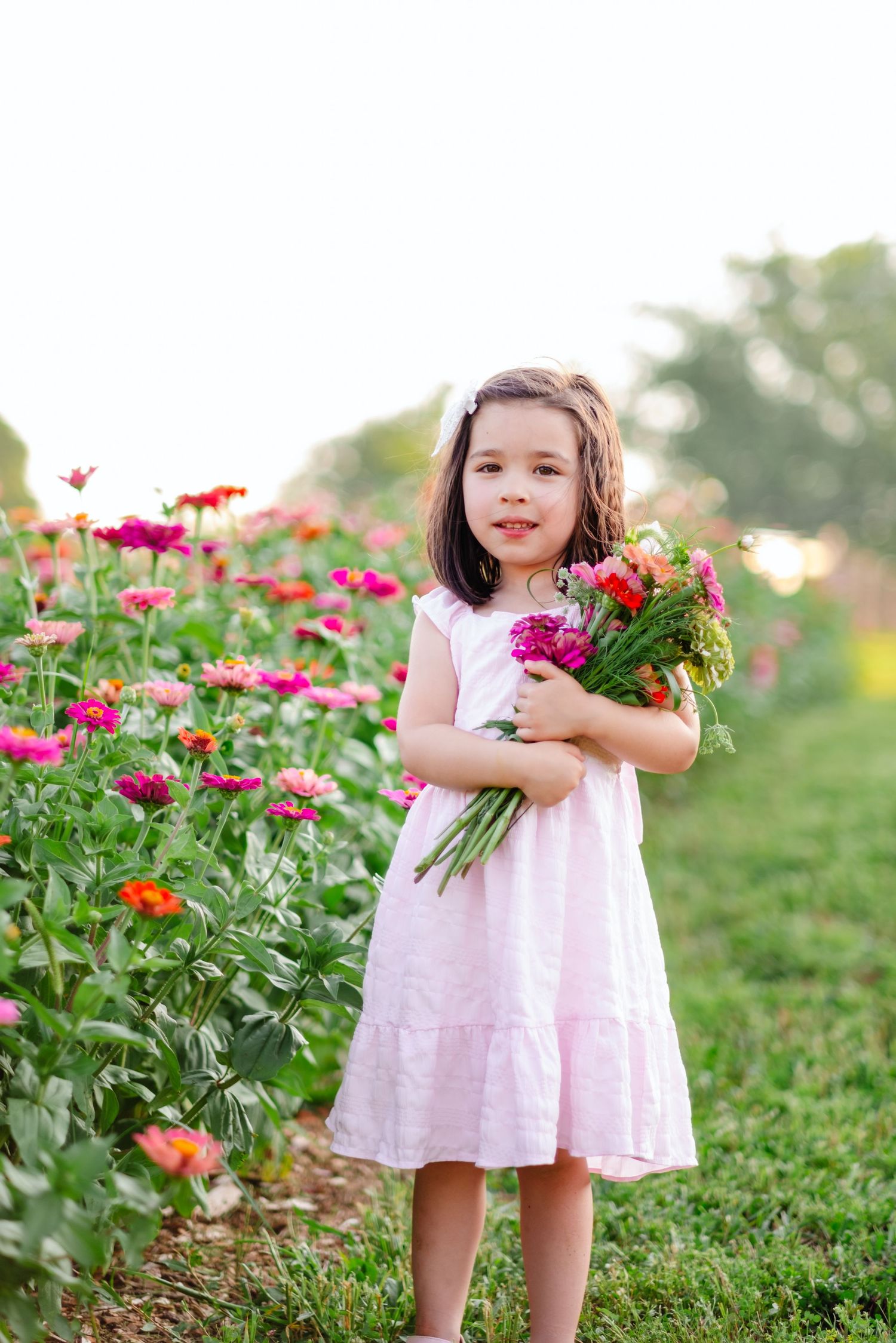 Young girl in pink dress holding colorful flower bouquet in a vibrant zinnia garden field.