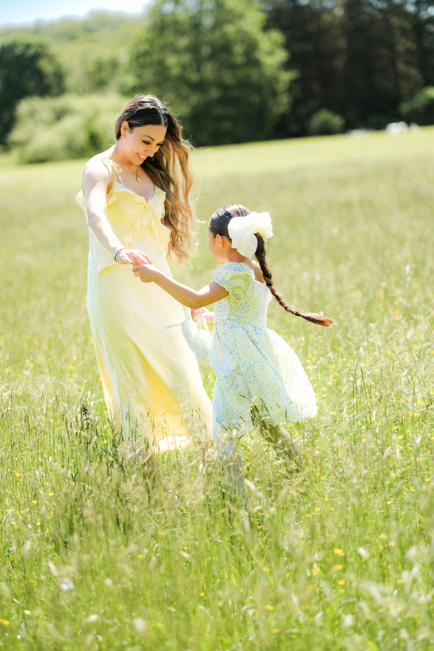 Mother and daughter in yellow dresses dancing in a sunny green meadow on a bright summer day.