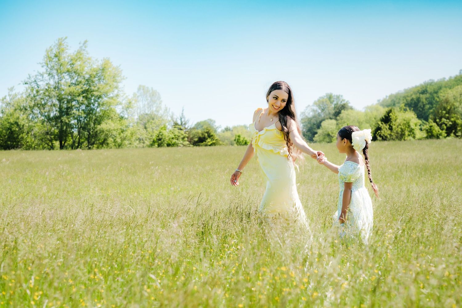 A family wearing white outfits walks together through a sunny meadow filled with tall grass and wildflowers.