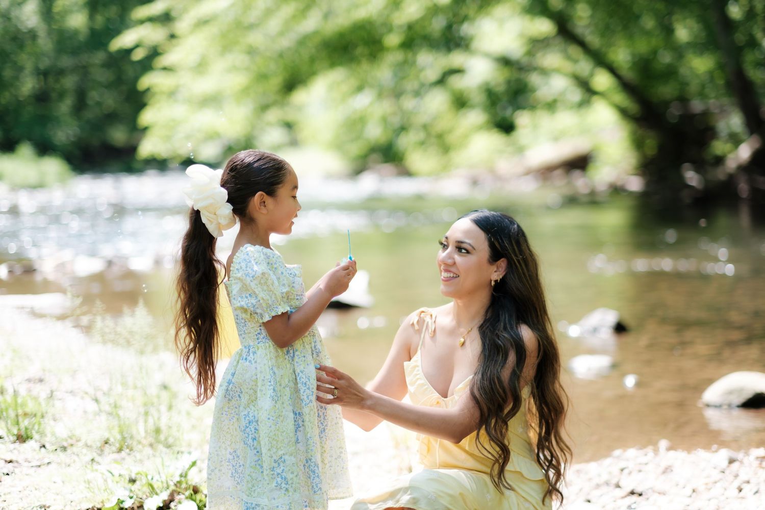 Two friends enjoying a picturesque picnic by a tranquil stream on a sunny summer afternoon.