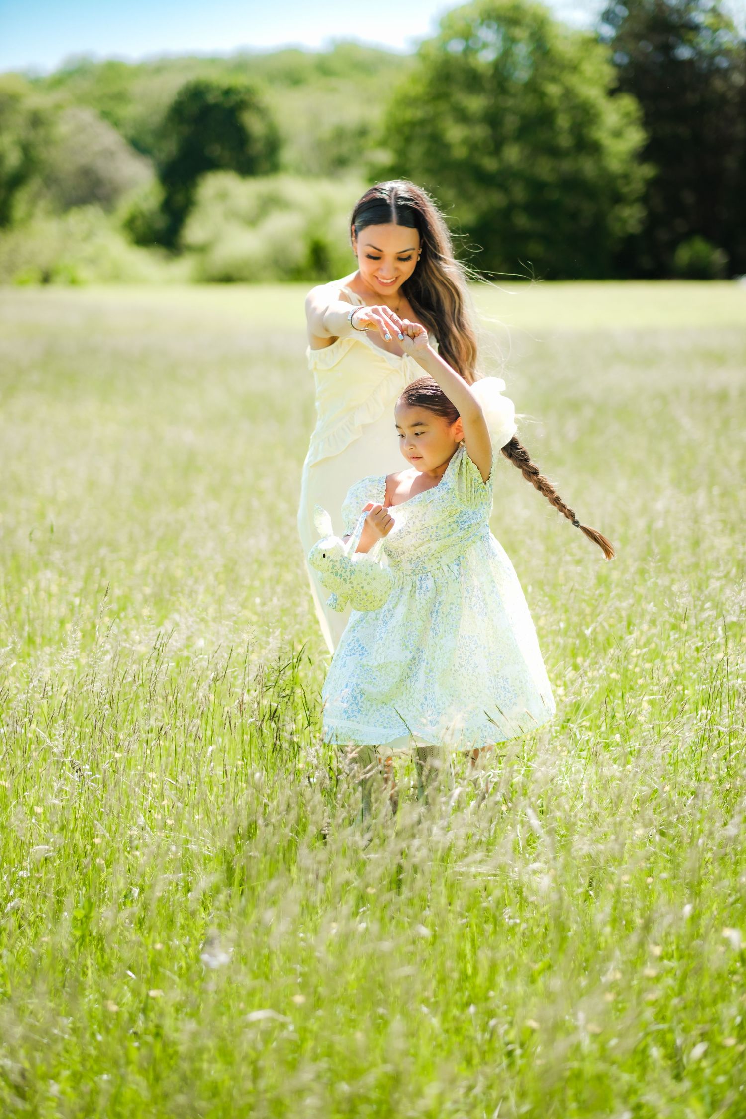 Mother and daughter in floral dresses dancing joyfully in a sunny green meadow.