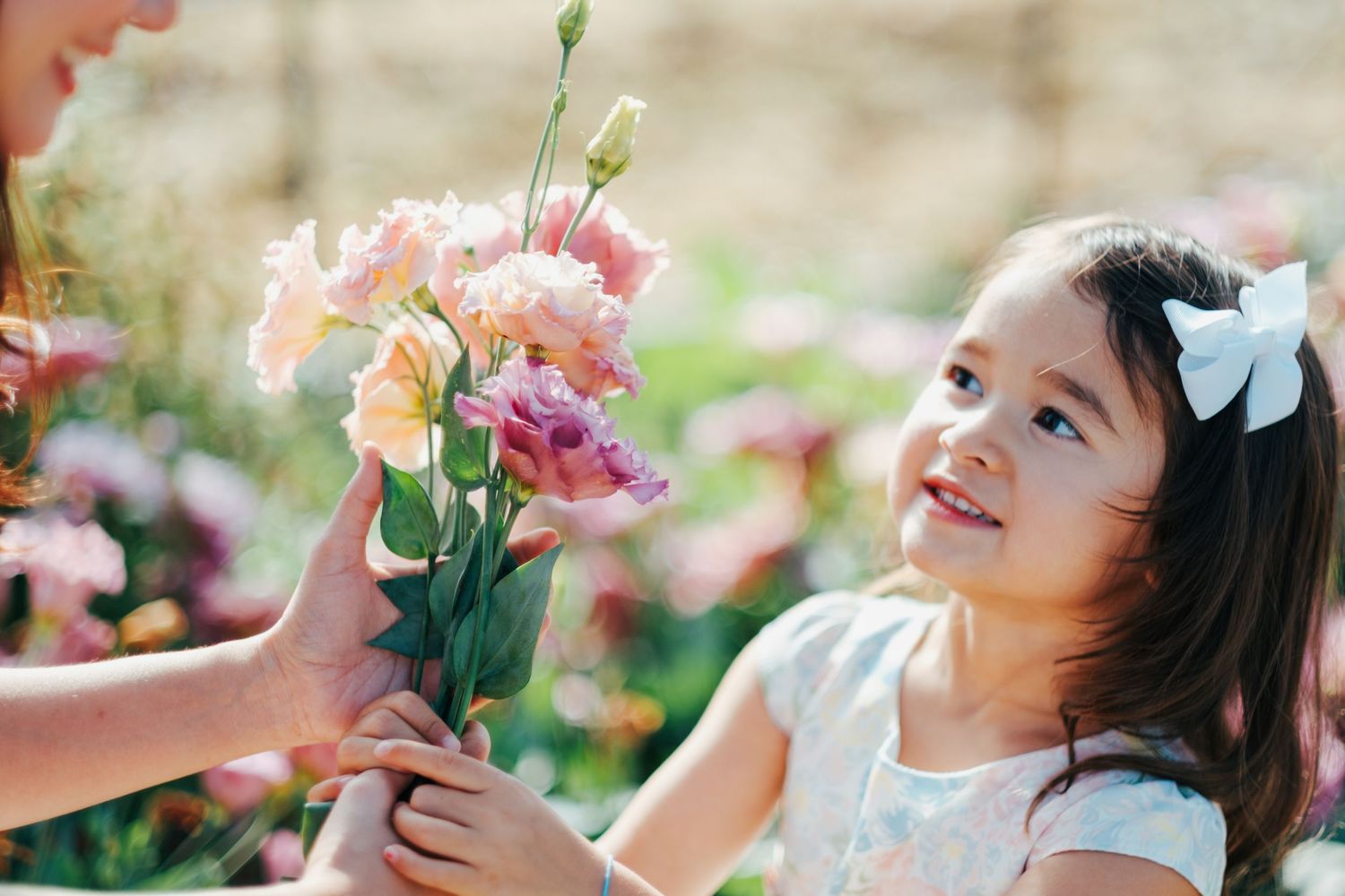 A young child in a white dress joyfully plays among blooming pink flowers in a garden setting.