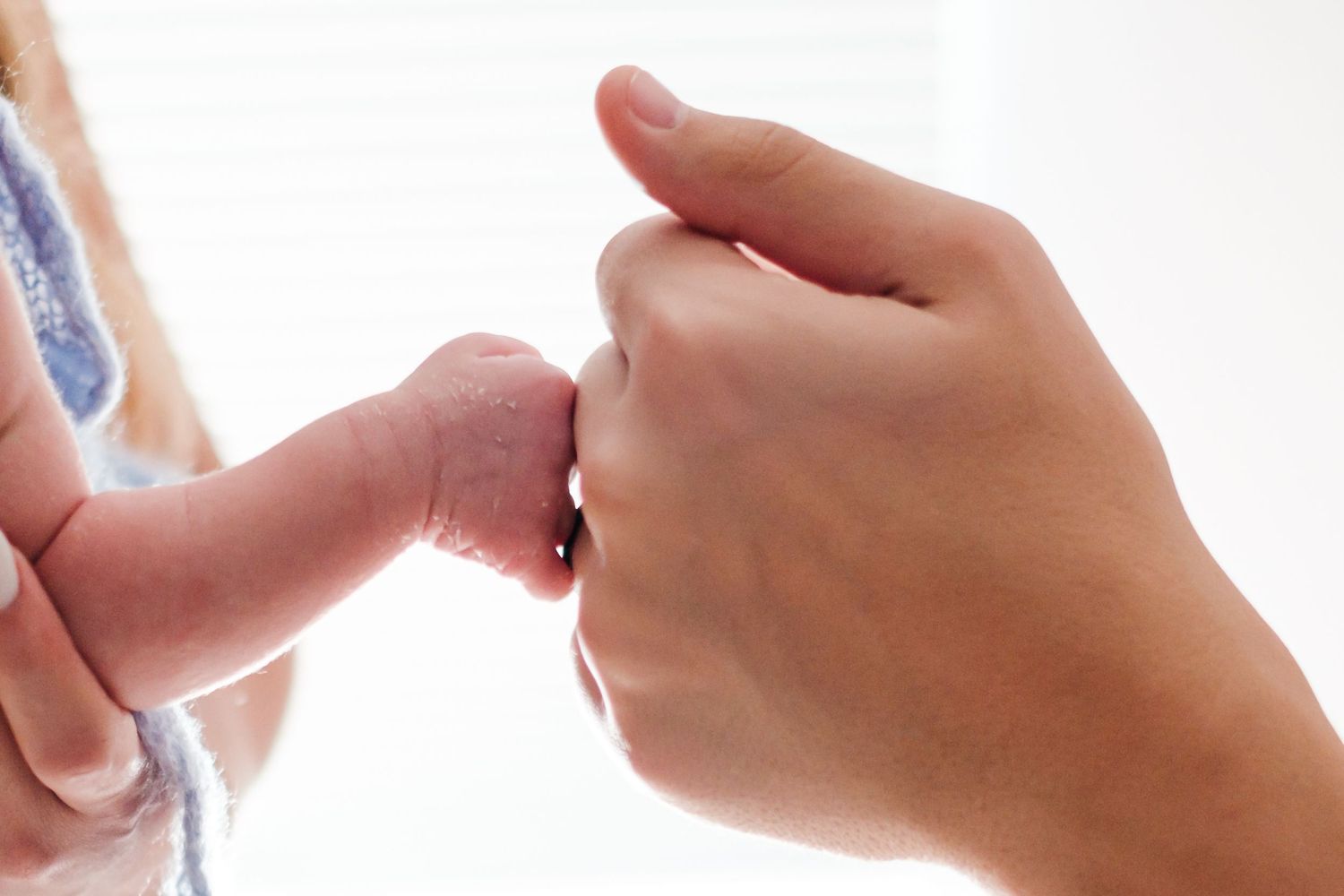 Close-up of an adult hand gently holding a newborn baby's tiny hand and foot.