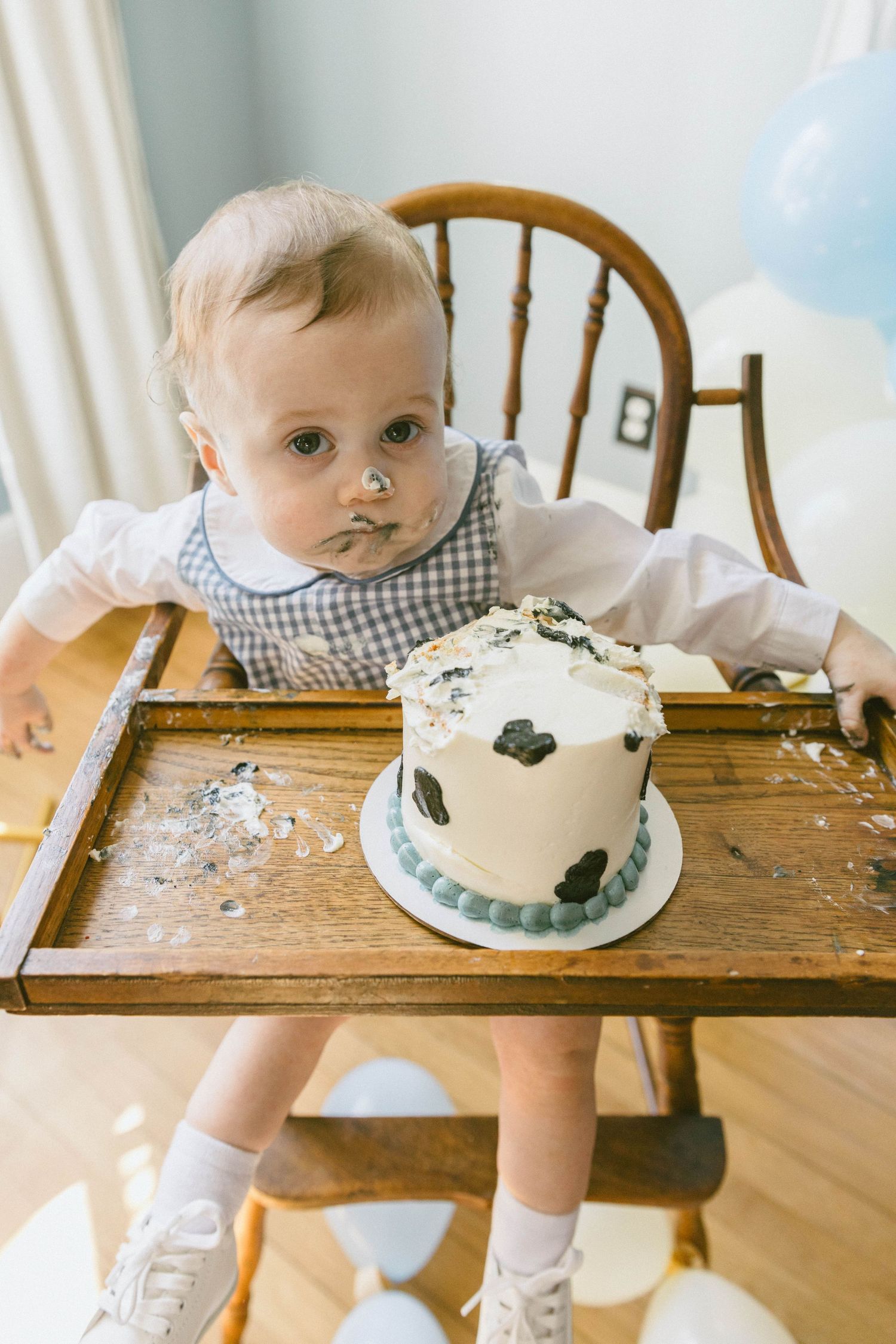 Baby in high chair with smashed first birthday cake on tray, face covered in frosting, celebrating milestone.