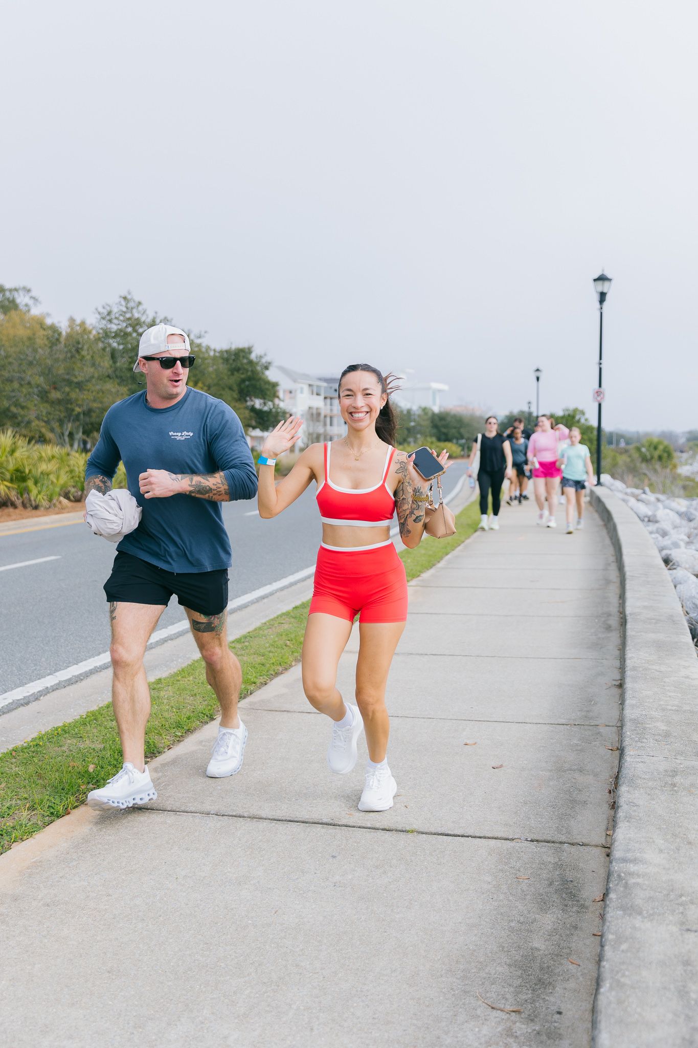 Two people in athletic wear jogging together on a paved coastal path during daytime exercise.